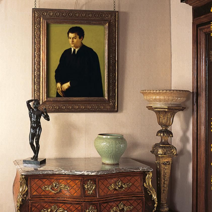 Elegant antique interior with portrait painting, bronze statue, ceramic vase, and ornate wooden furniture.