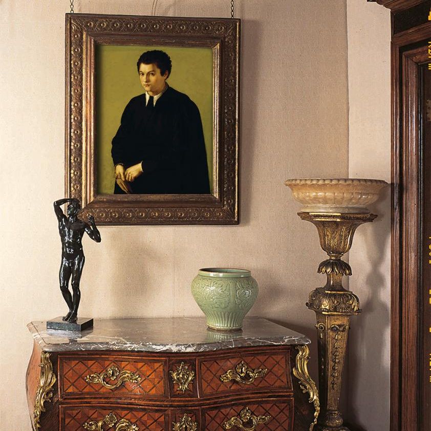 Elegant antique interior with portrait painting, bronze statue, ceramic vase, and ornate wooden furniture.
