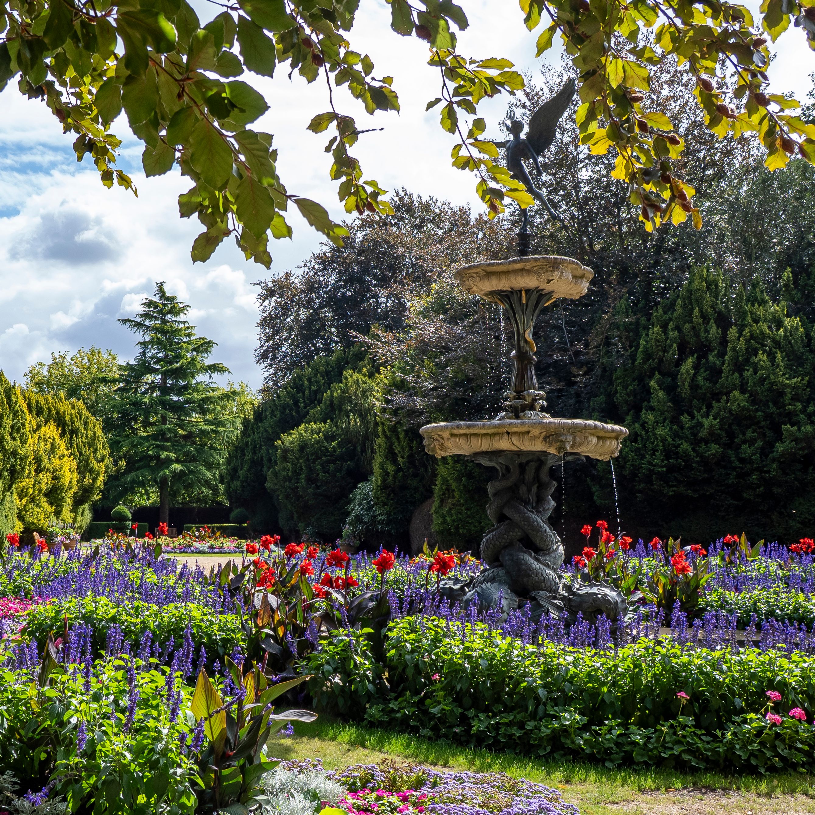 Decorative fountain surrounded by vibrant flower beds and greenery in a garden.