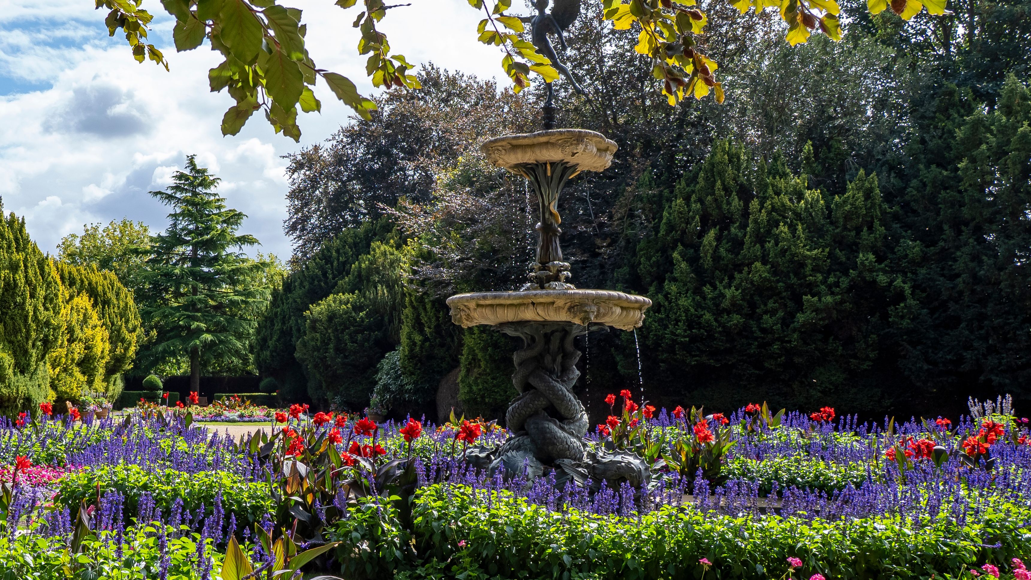 Decorative fountain surrounded by vibrant flower beds and greenery in a garden.