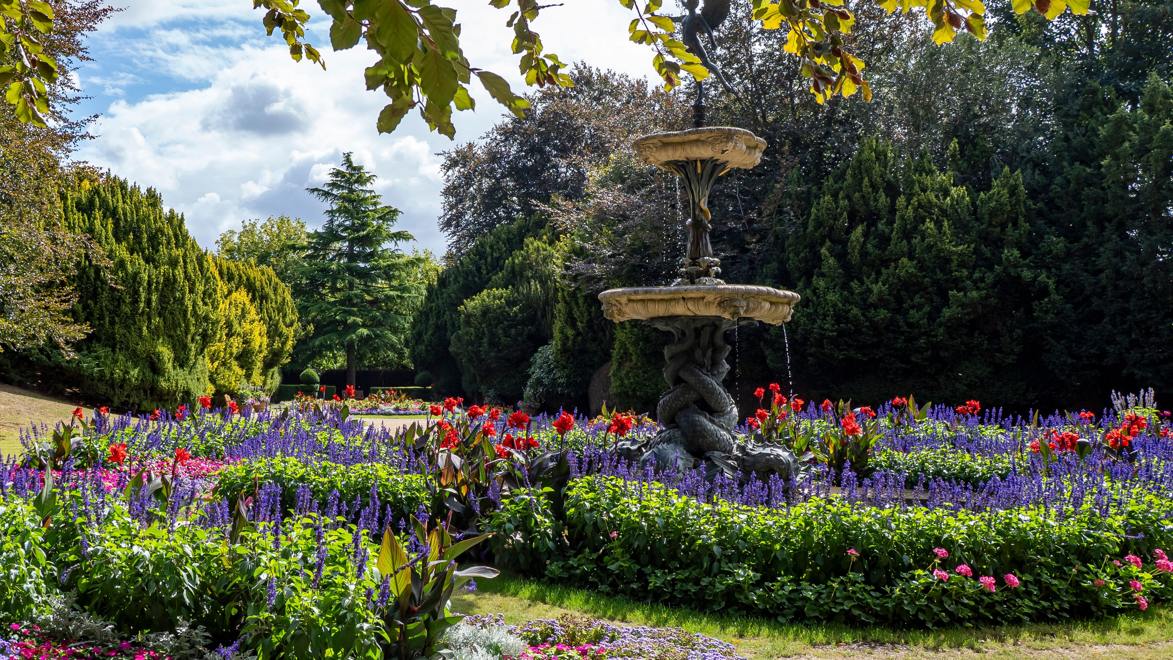 Decorative fountain surrounded by vibrant flower beds and greenery in a garden.