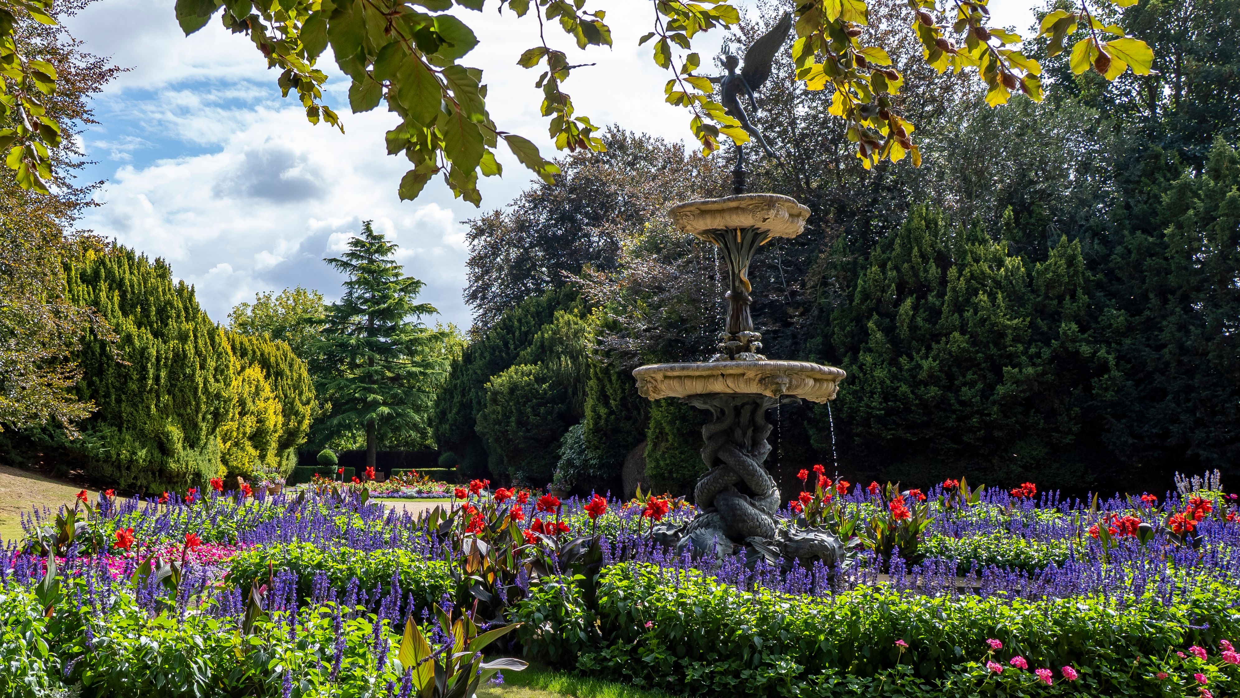 Decorative fountain surrounded by vibrant flower beds and greenery in a garden.