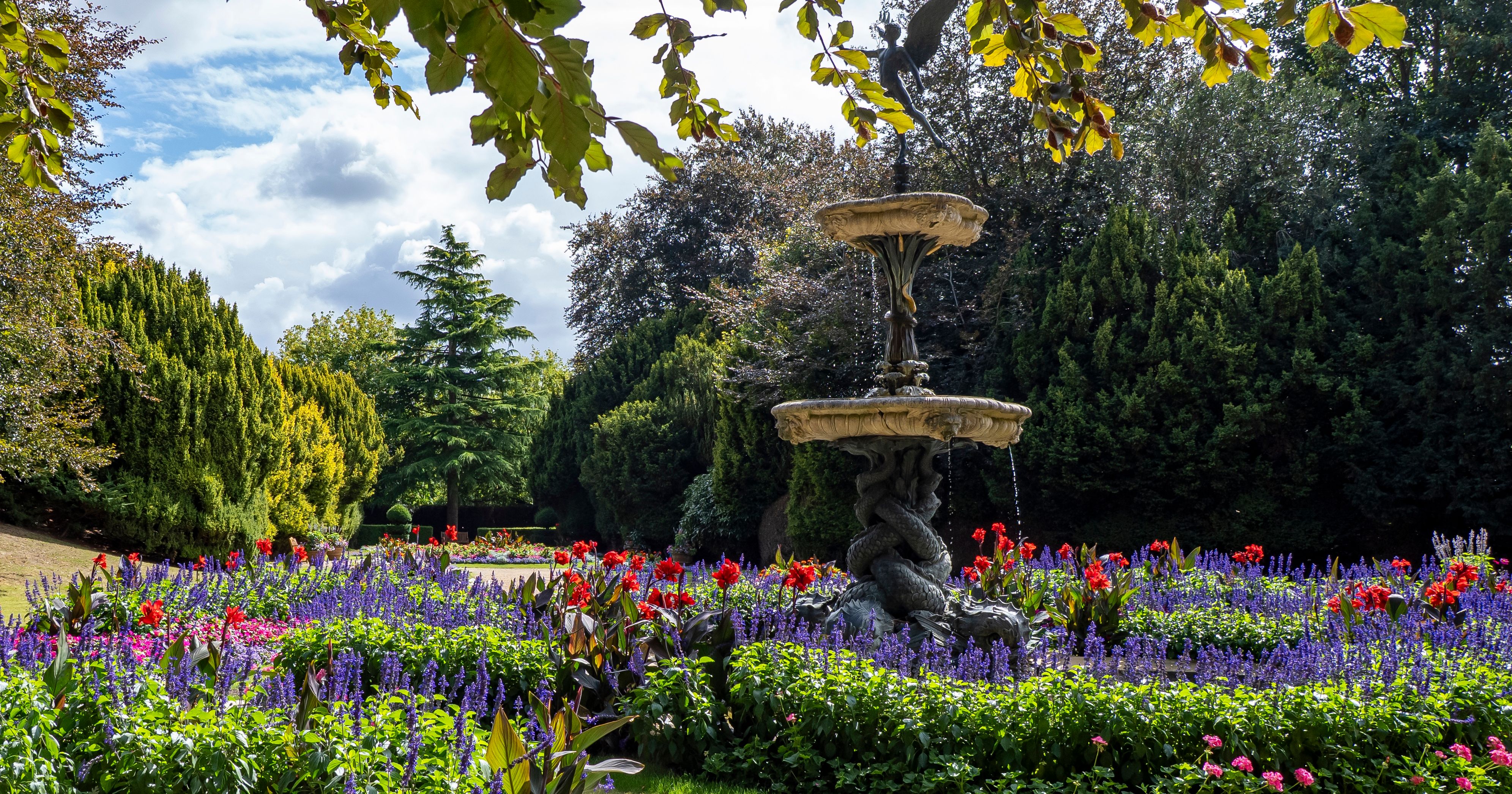 Decorative fountain surrounded by vibrant flower beds and greenery in a garden.