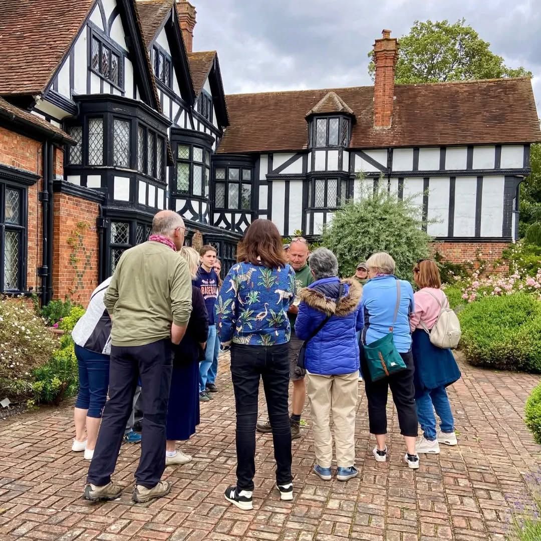 A group of people gathered outside a Tudor-style building on a brick pathway.