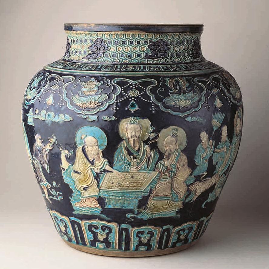 Large Chinese ceramic jar with intricate blue, green, and gold designs depicting figures in traditional attire