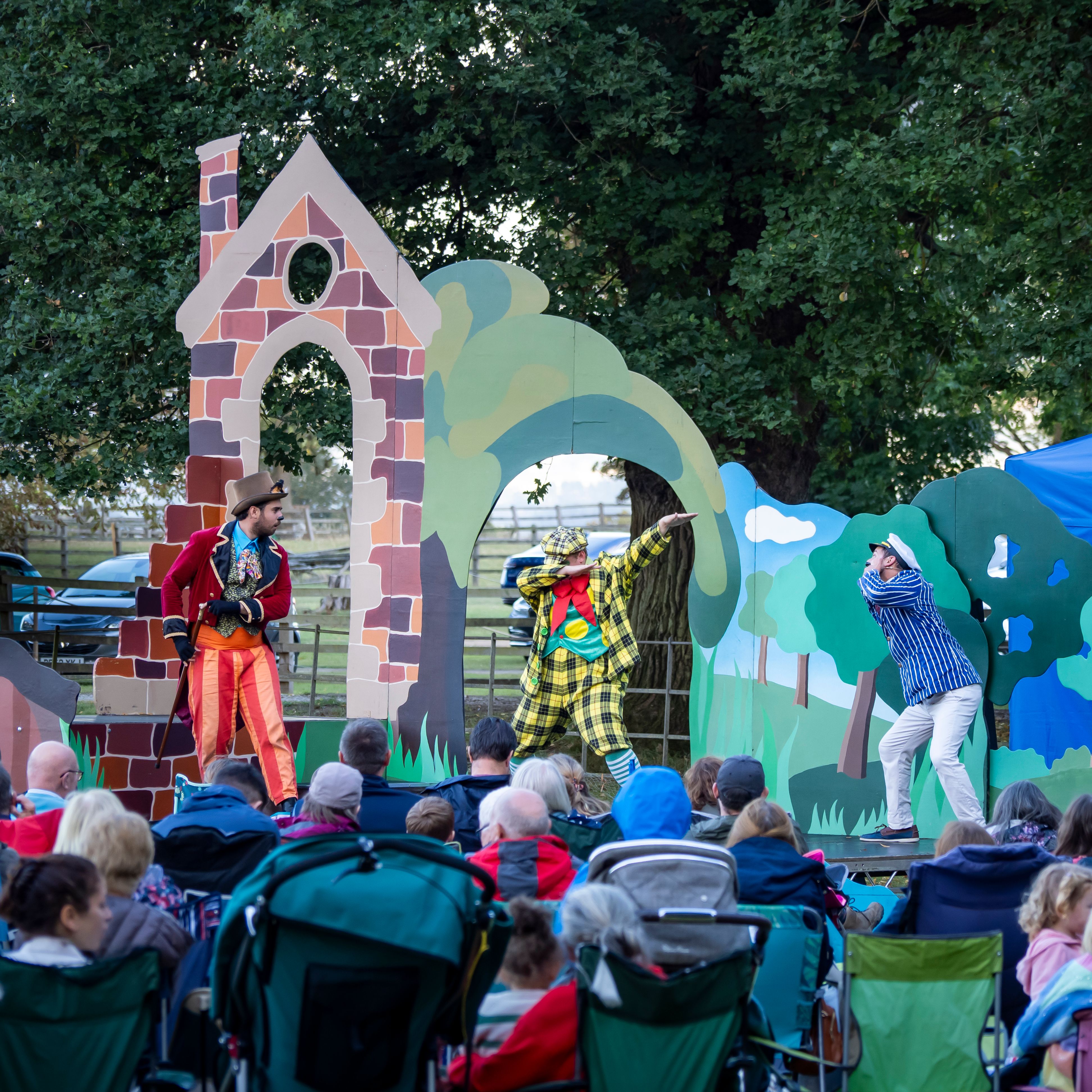 Outdoor theater performance with actors in colorful costumes entertaining a seated audience.