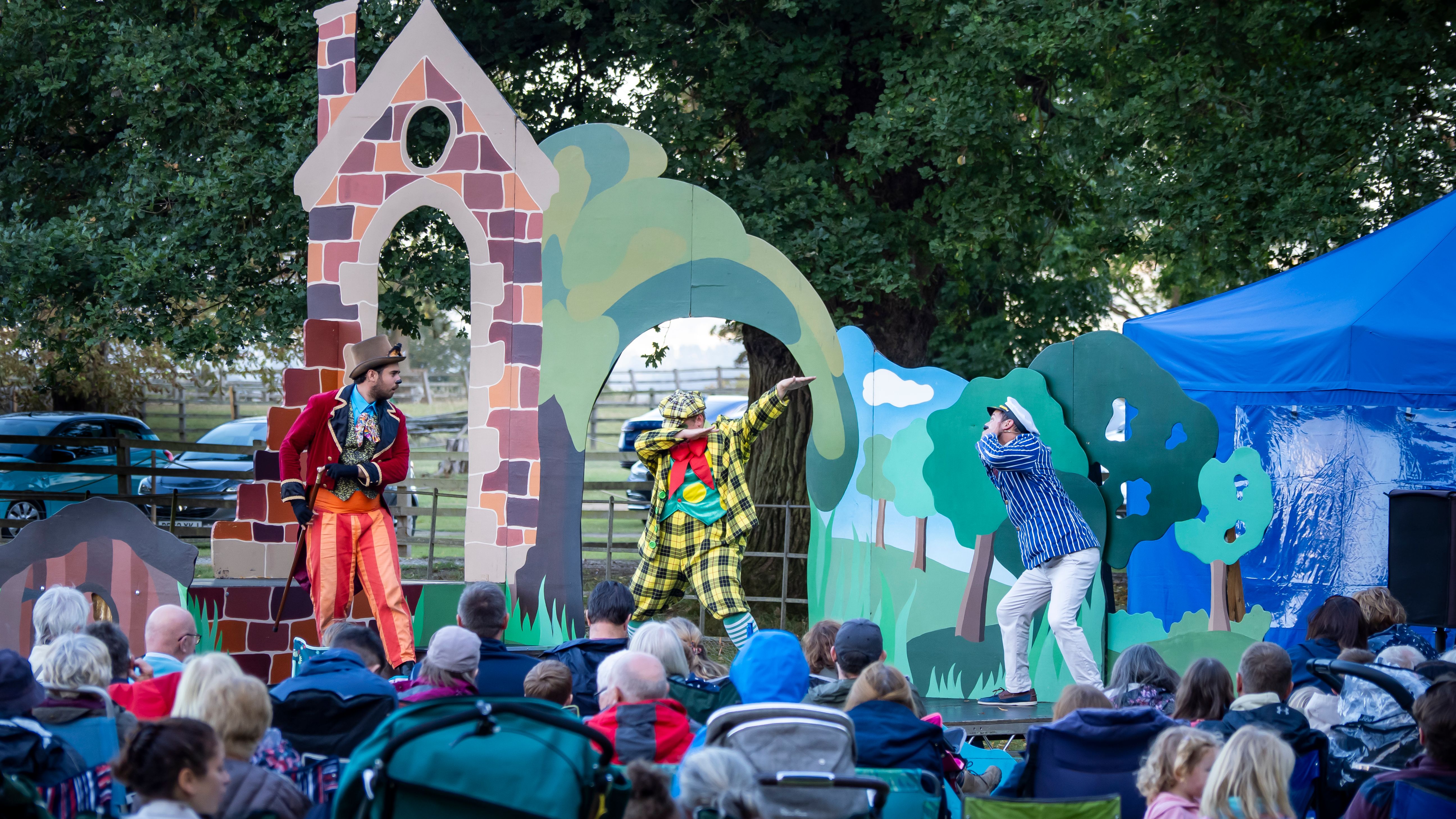 Outdoor theater performance with actors in colorful costumes entertaining a seated audience.