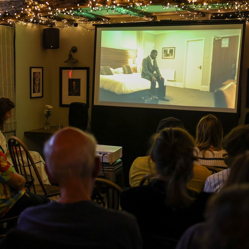 Audience watching a film in a cozy, dimly-lit room with string lights and a projector screen