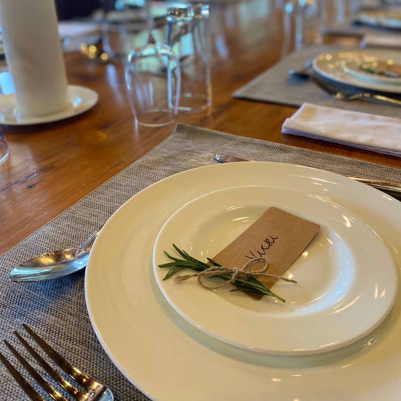 Elegant table setting with white plates, cutlery, a candle, and name card tied with herbs.