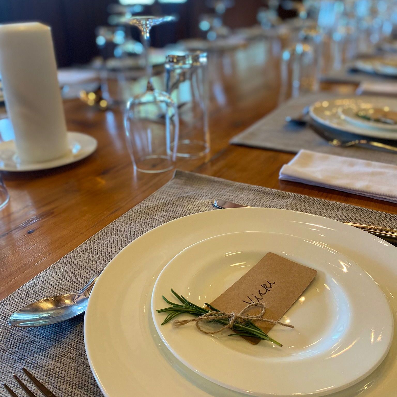 Elegant table setting with white plates, cutlery, a candle, and name card tied with herbs.