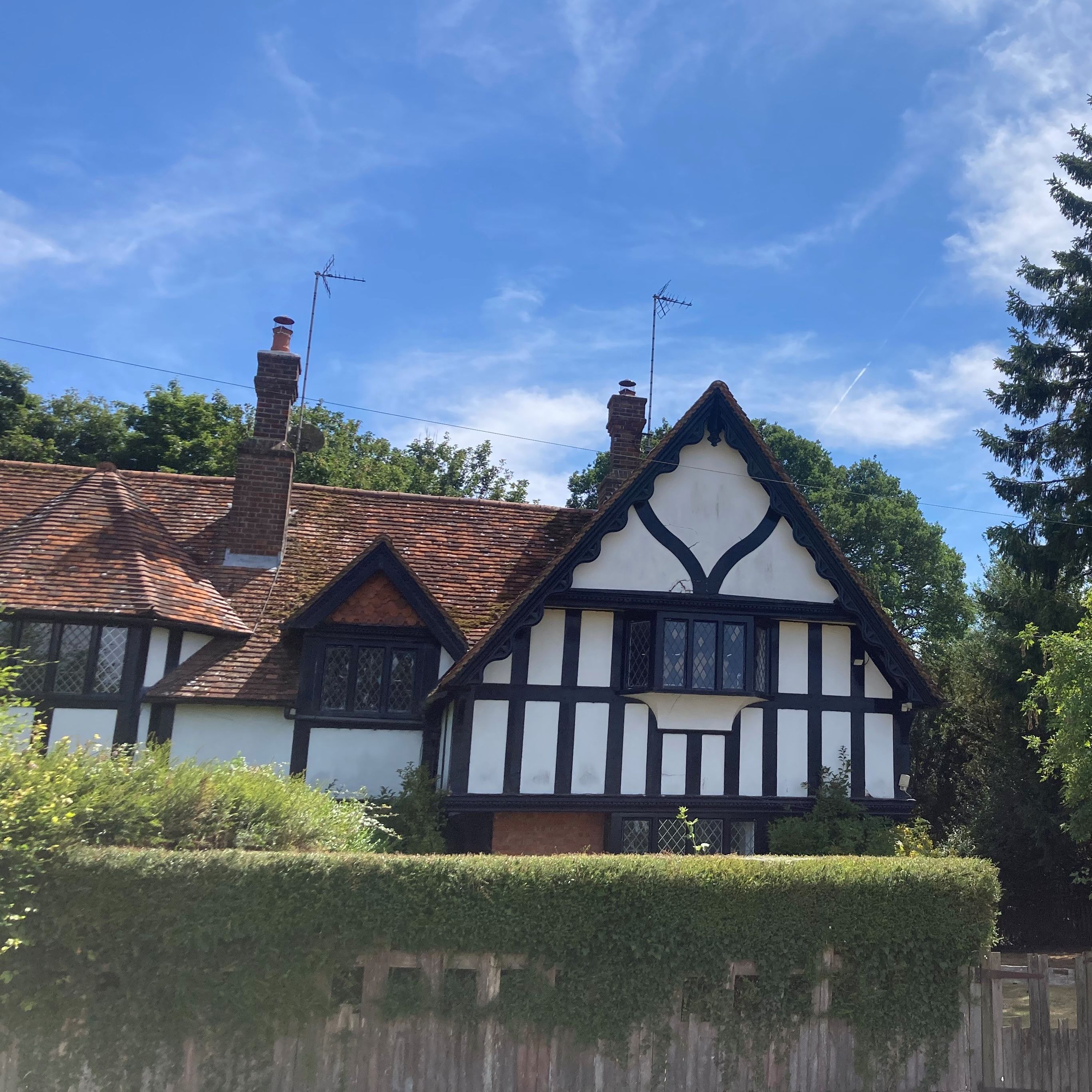 Traditional Tudor-style house with timber framing, surrounded by greenery under a blue sky.