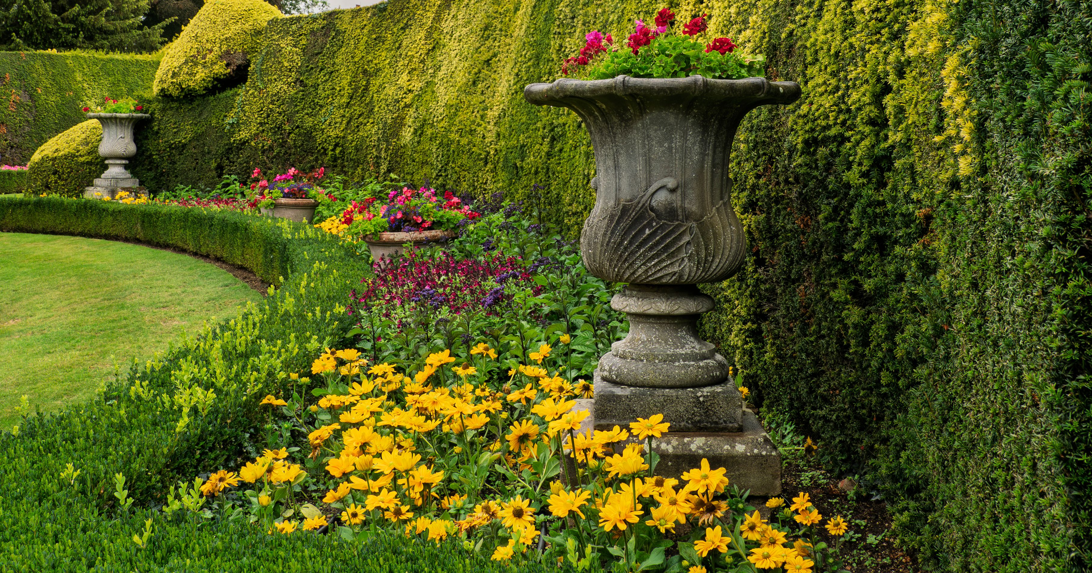 Beautiful formal garden with trimmed hedges, colorful flowers, and decorative stone urns.
