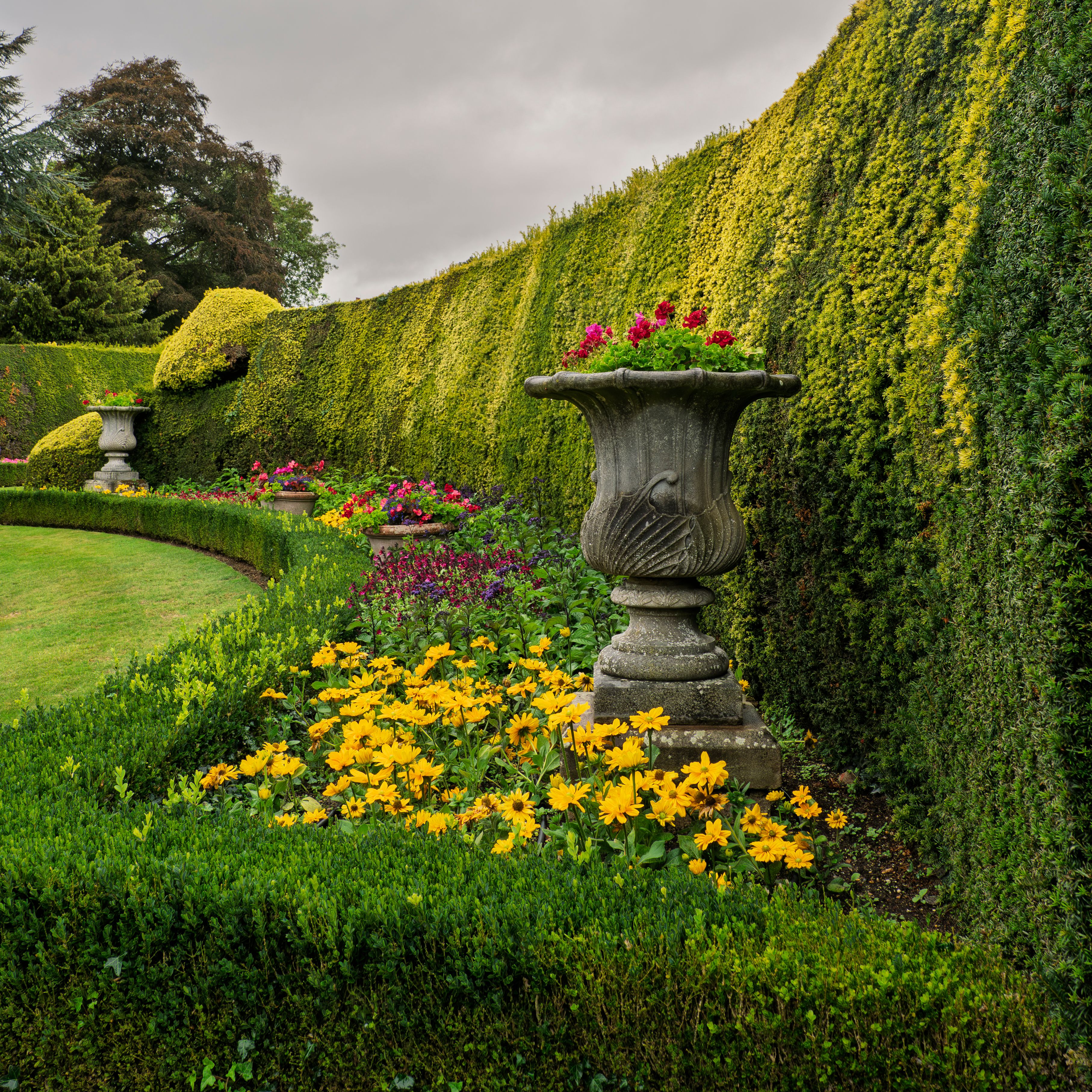 Beautiful formal garden with trimmed hedges, colorful flowers, and decorative stone urns.