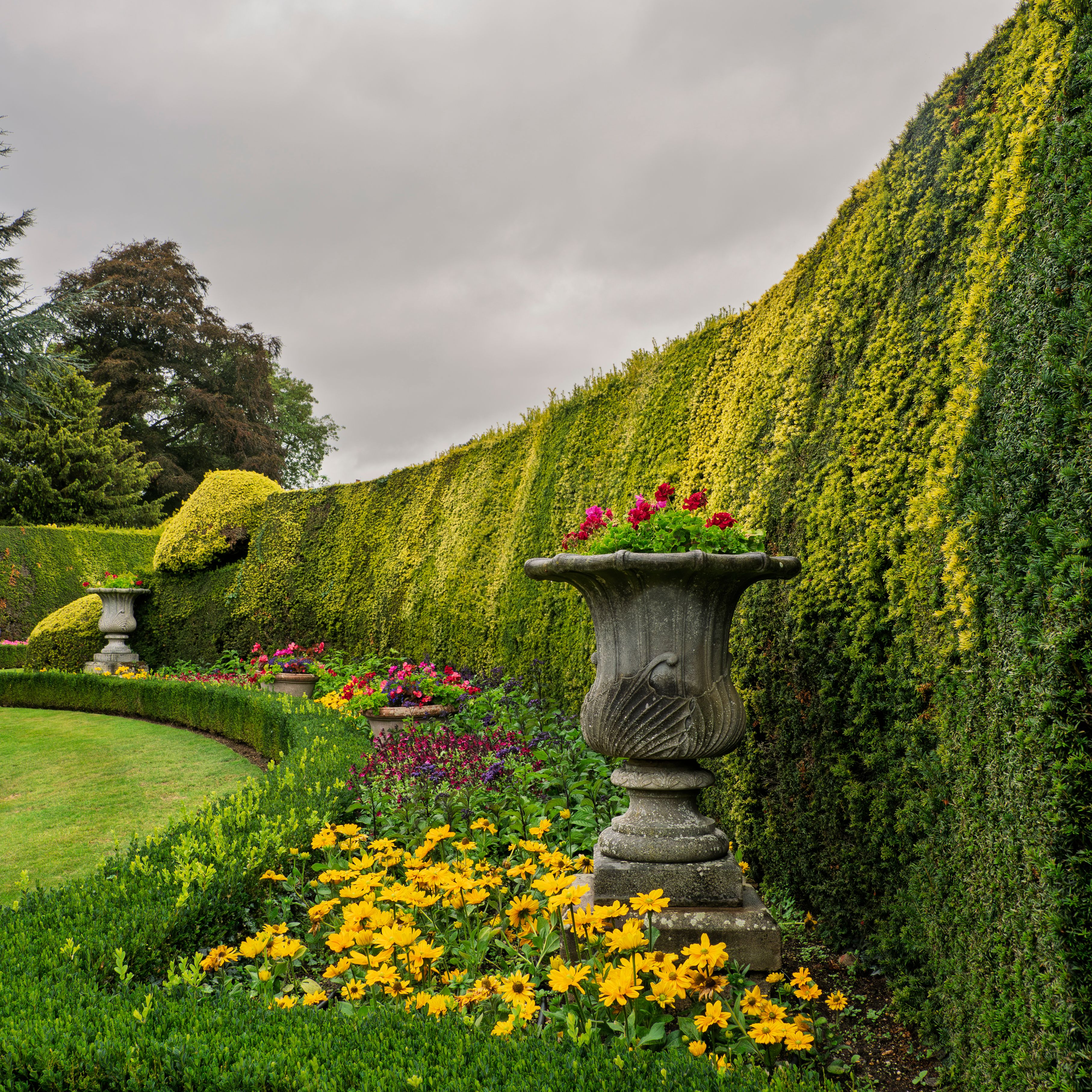 Beautiful formal garden with trimmed hedges, colorful flowers, and decorative stone urns.