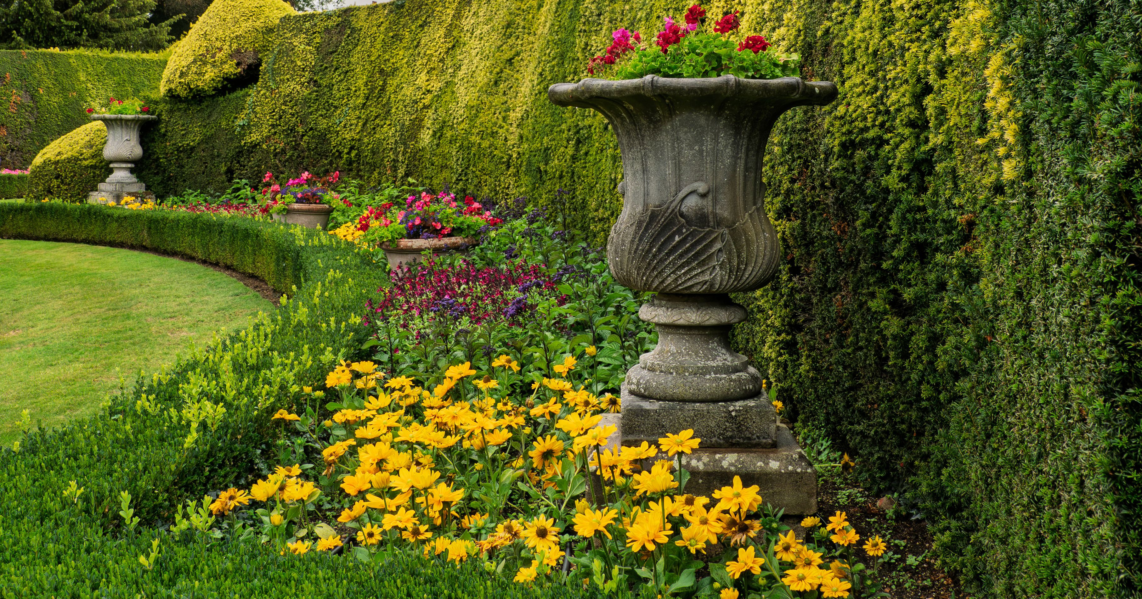 Beautiful formal garden with trimmed hedges, colorful flowers, and decorative stone urns.