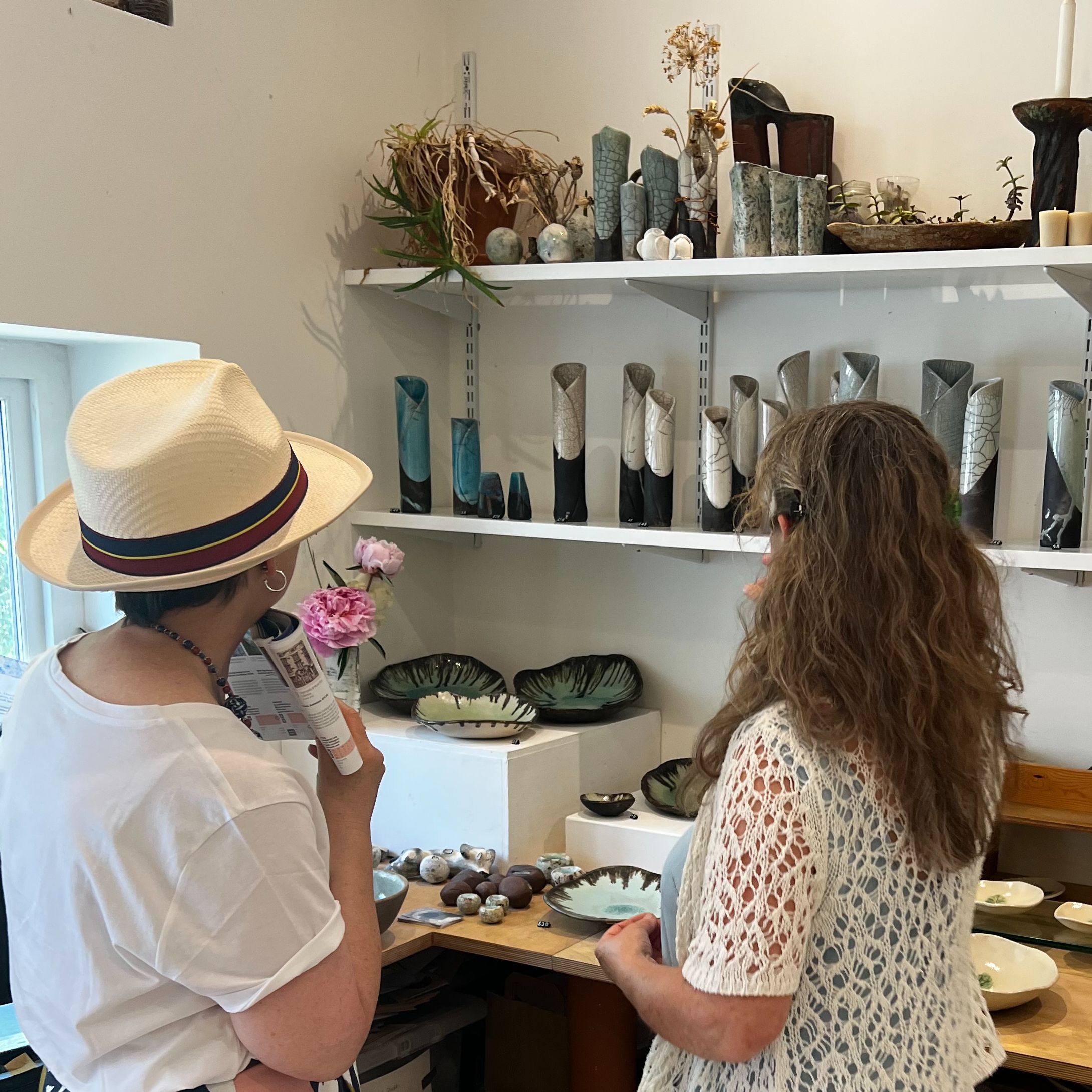Two women looking at ceramics and pottery displayed on shelves in a studio or shop.