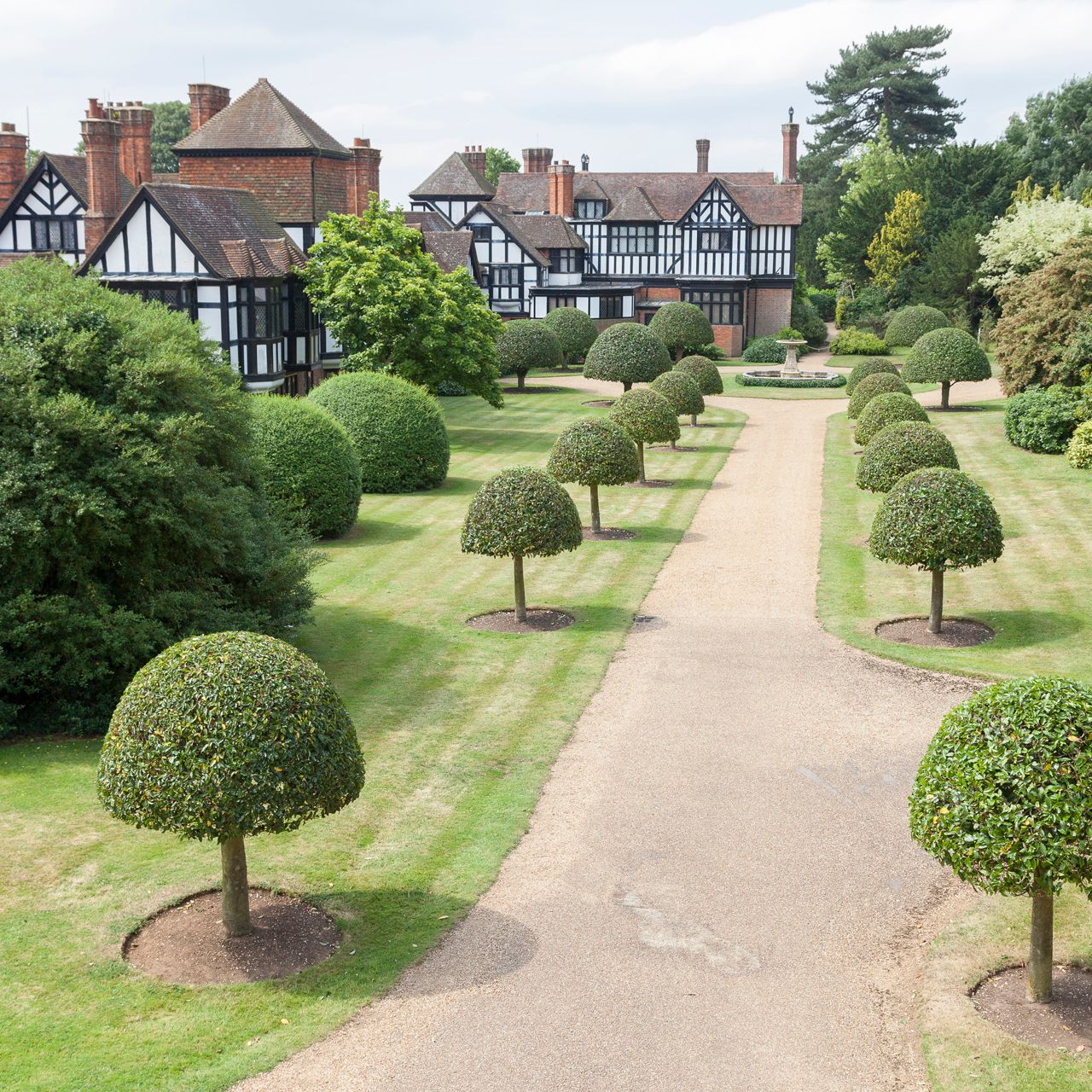 Formal garden with trimmed trees and a Tudor-style manor house in the background