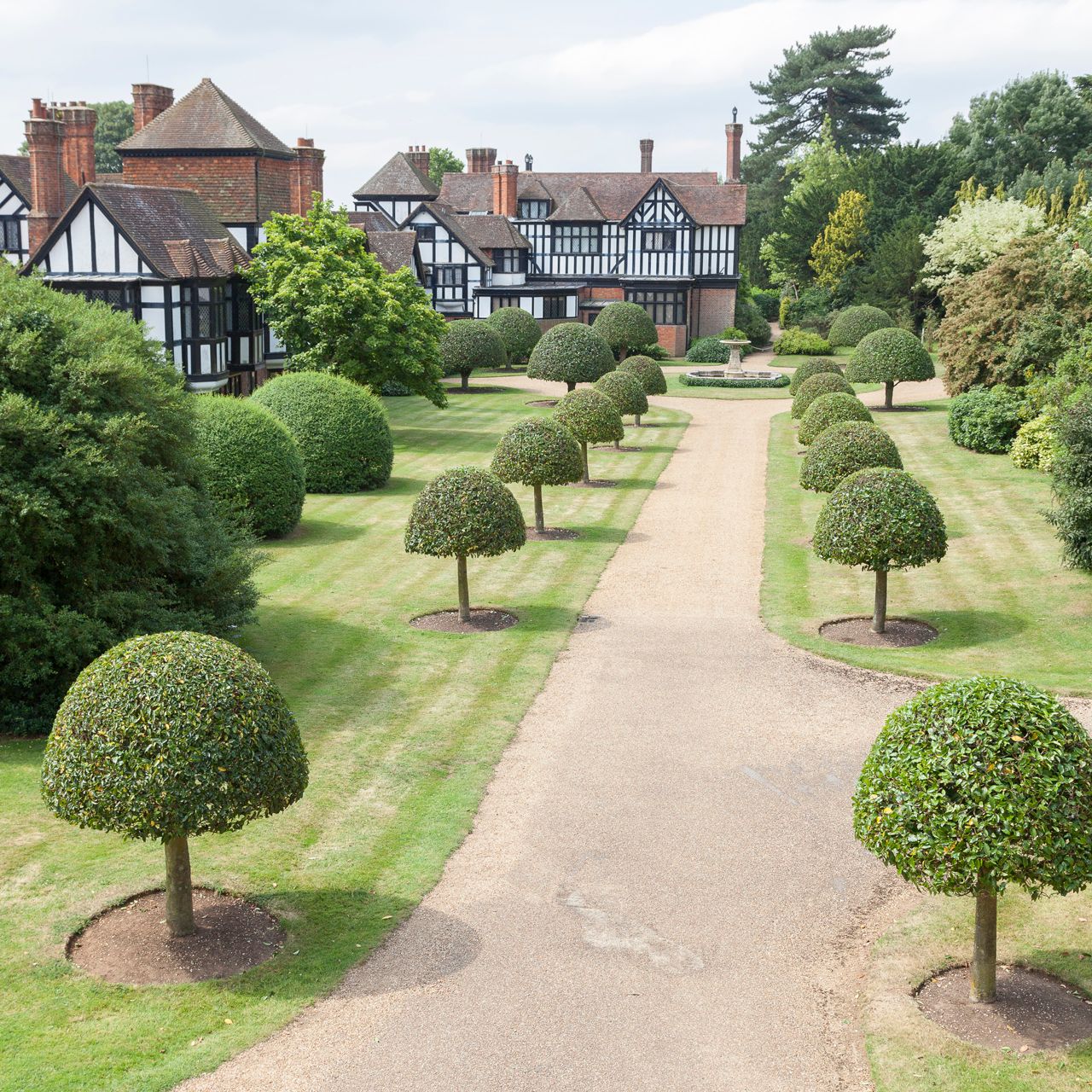 Formal garden with trimmed trees and a Tudor-style manor house in the background