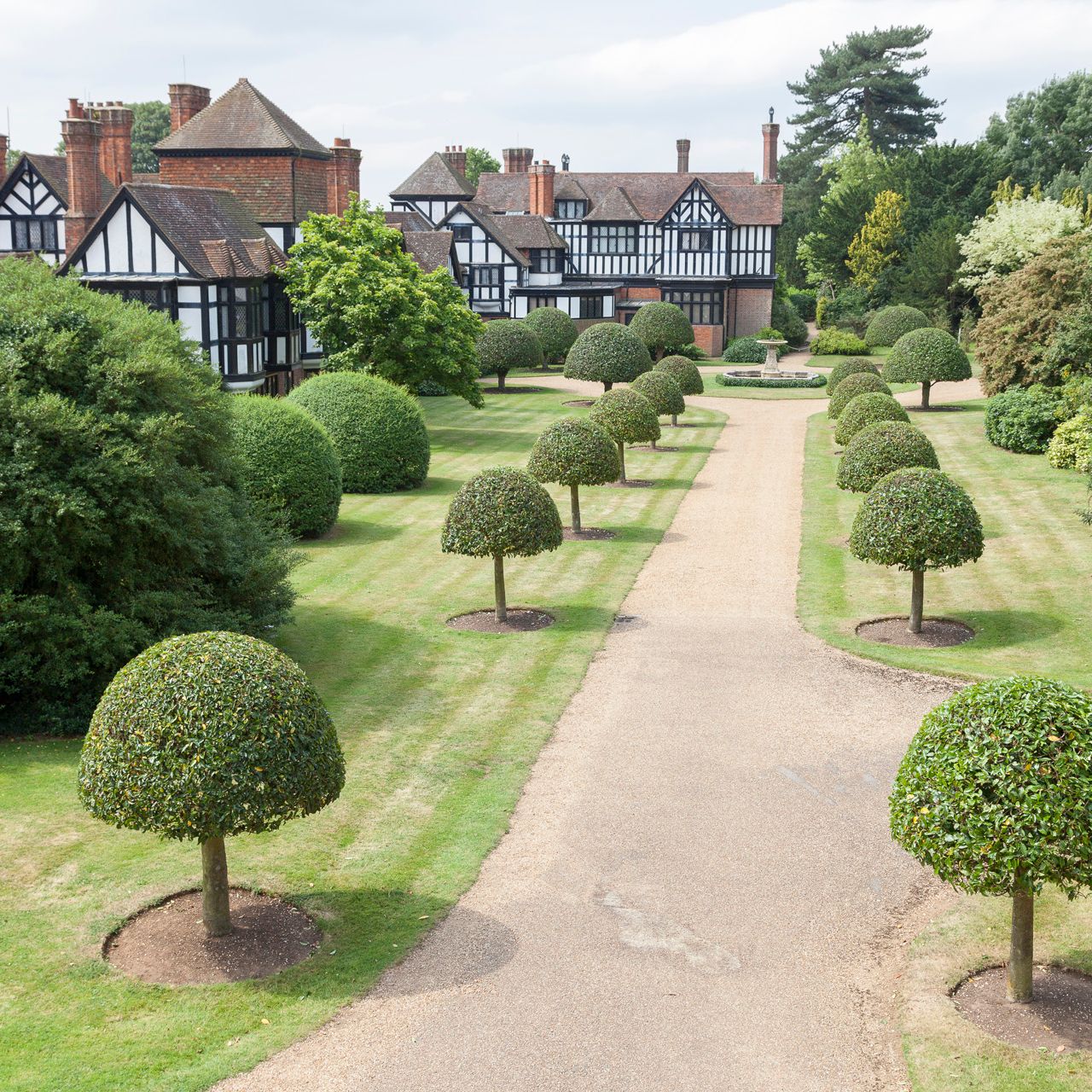 Formal garden with trimmed trees and a Tudor-style manor house in the background