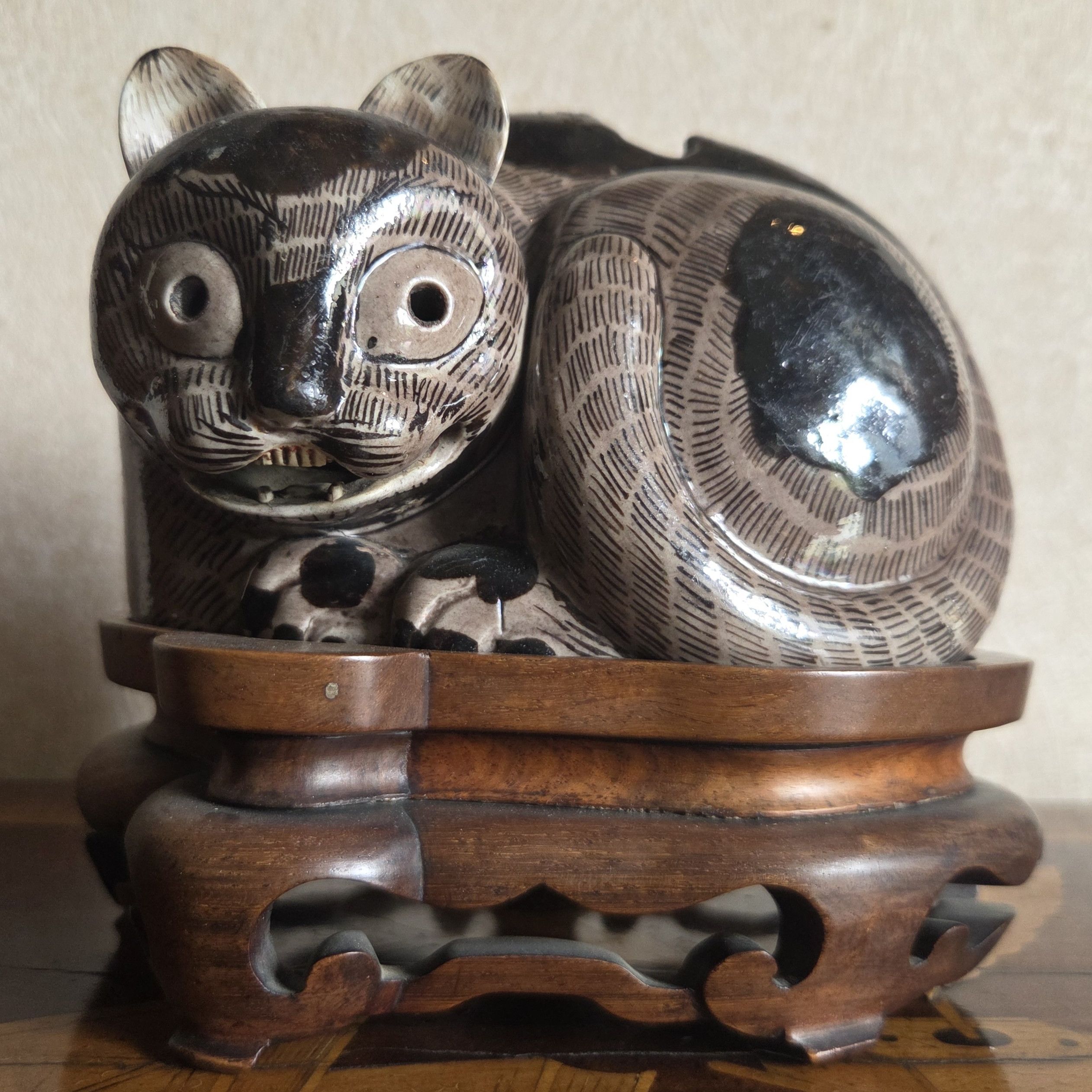Close-up of a striped ceramic cat figurine on a carved wooden stand