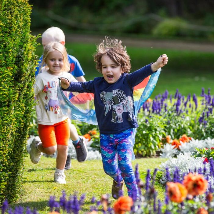 Children running through a sunny garden beside colourful flowerbeds