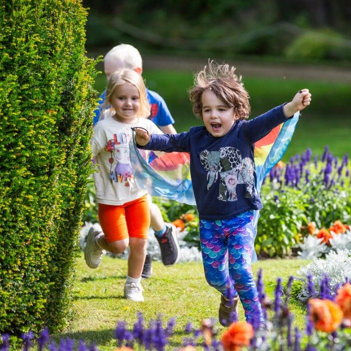 Children running through a sunny garden beside colourful flowerbeds