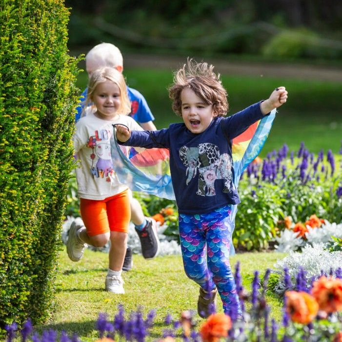 Children running through a sunny garden beside colourful flowerbeds