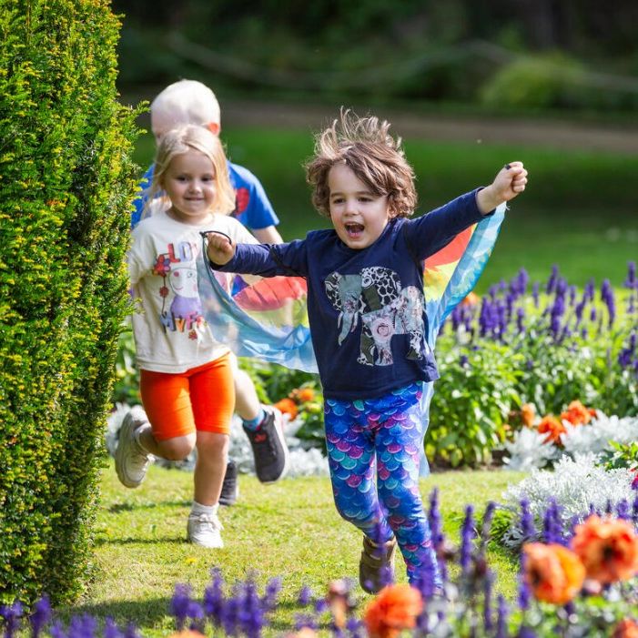Children running through a sunny garden beside colourful flowerbeds