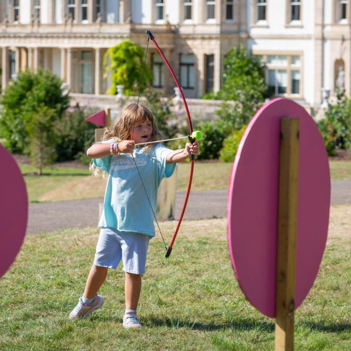 Child aiming a bow and arrow during an outdoor archery activity on a grassy lawn
