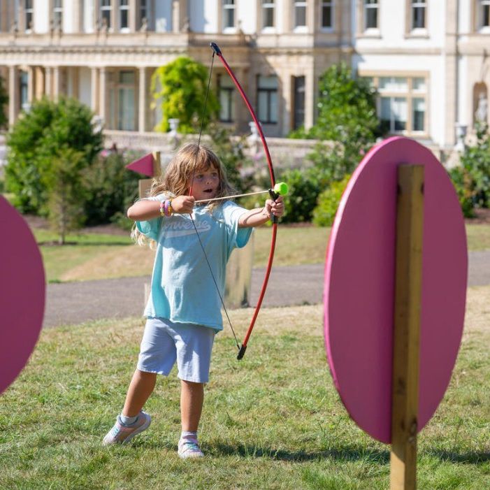 Child aiming a bow and arrow during an outdoor archery activity on a grassy lawn
