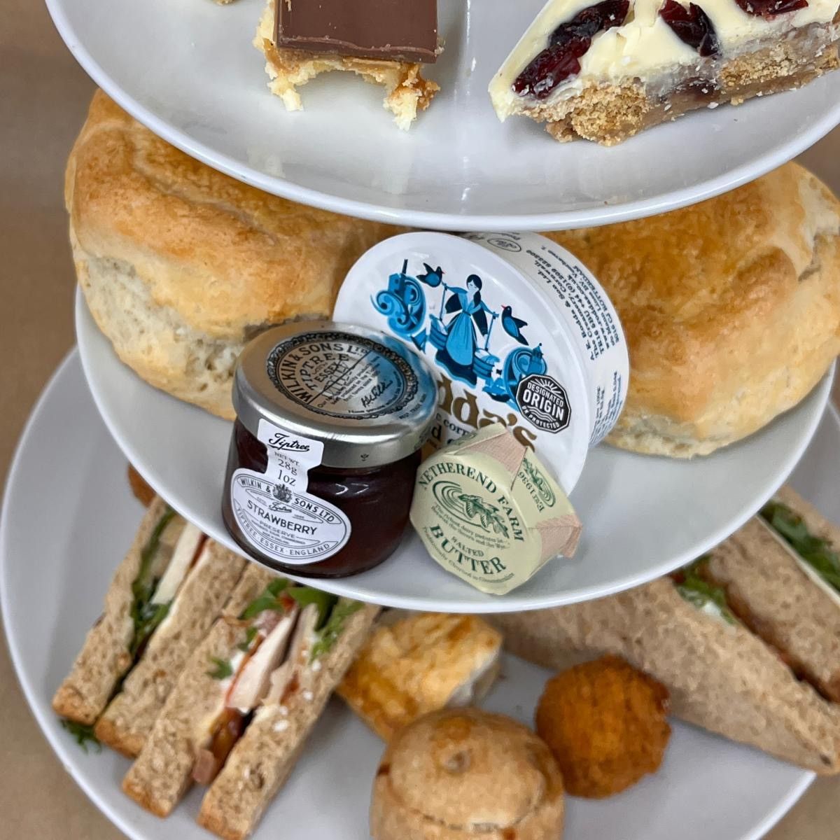 Three-tier afternoon tea stand with sandwiches, scones, jam, butter and assorted cakes