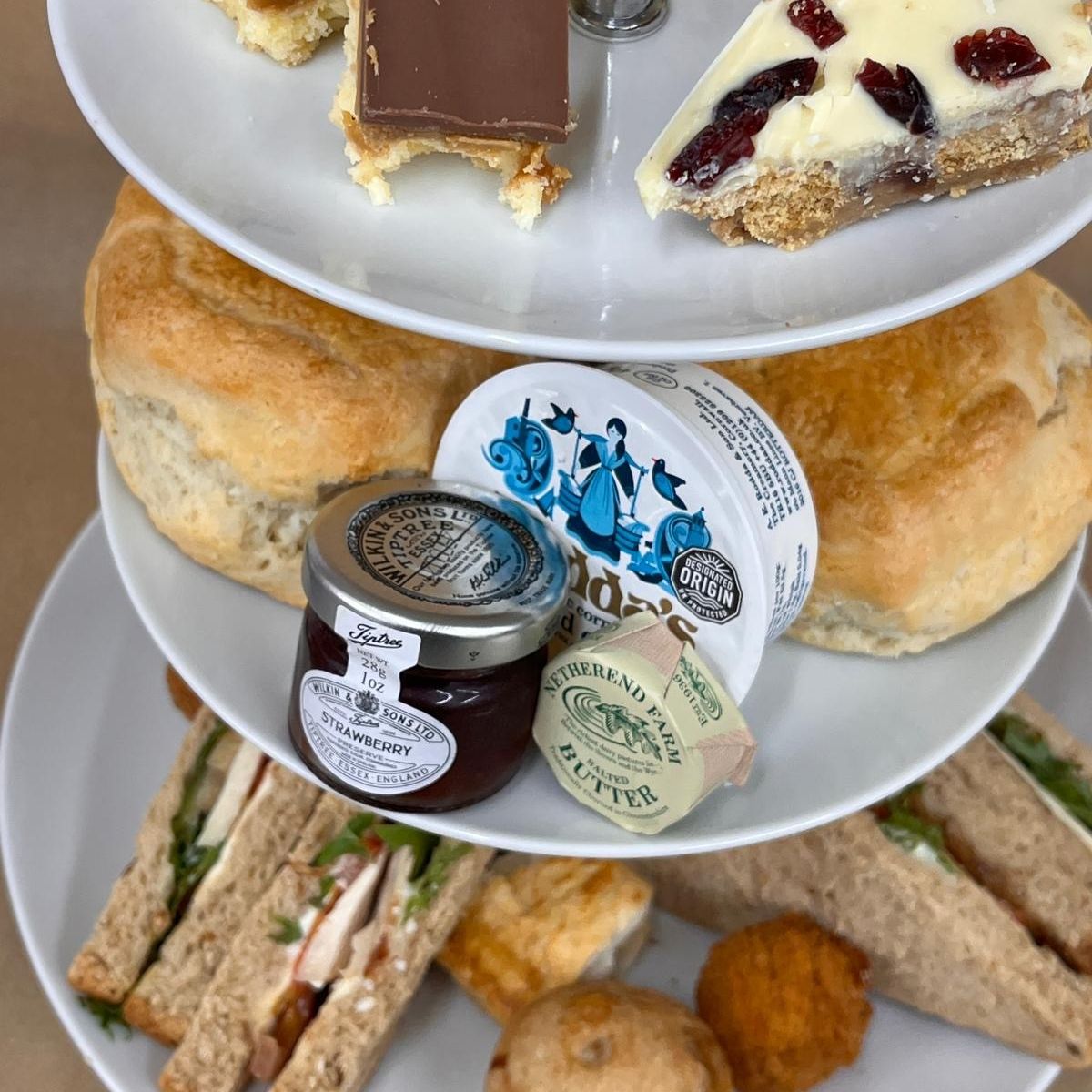 Three-tier afternoon tea stand with sandwiches, scones, jam, butter and assorted cakes