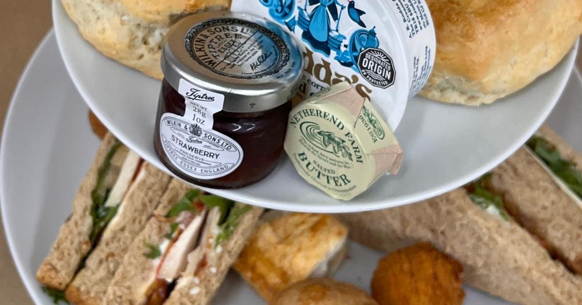 Three-tier afternoon tea stand with sandwiches, scones, jam, butter and assorted cakes