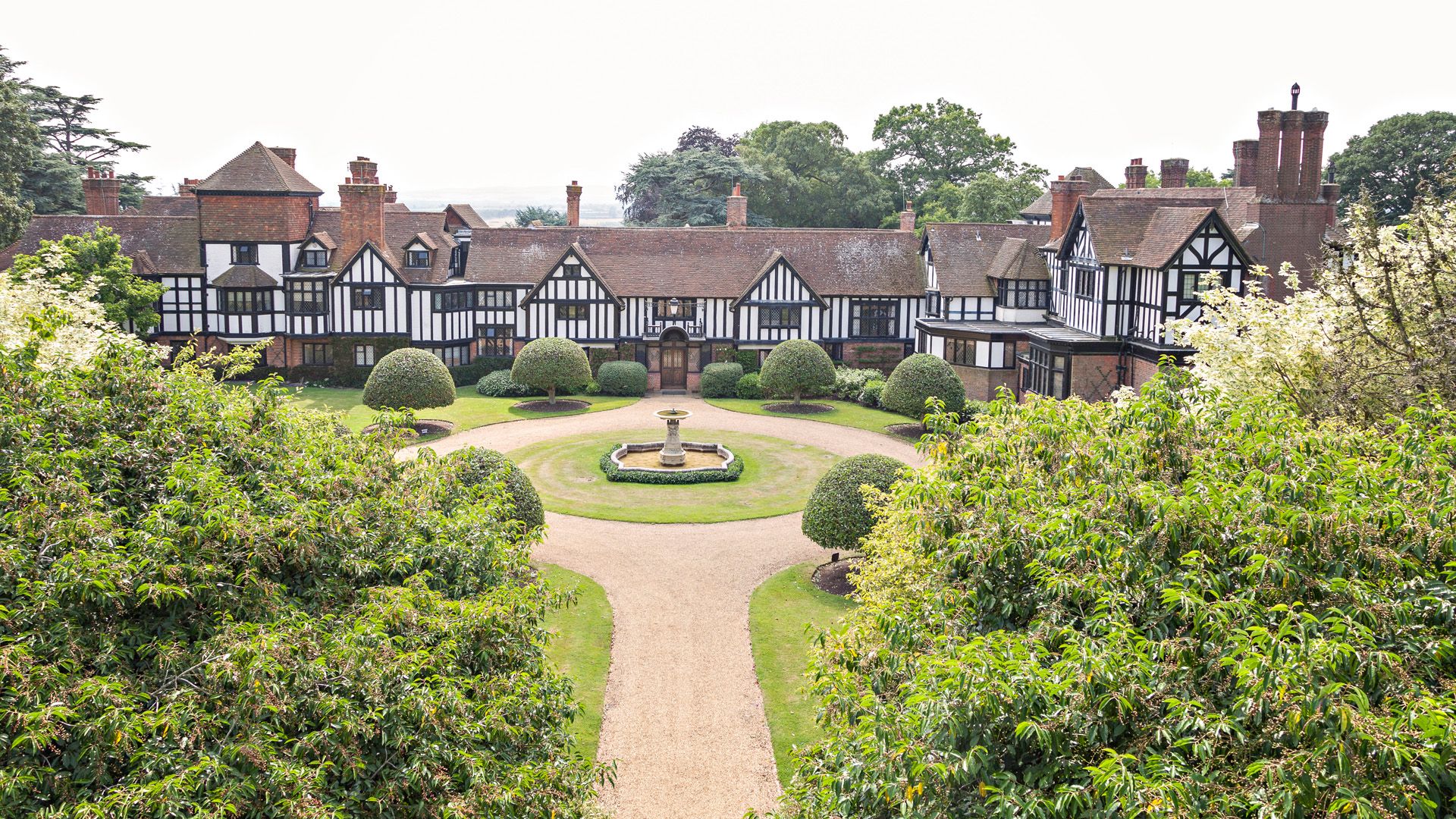 Large Tudor-style mansion with fountain and landscaped circular driveway
