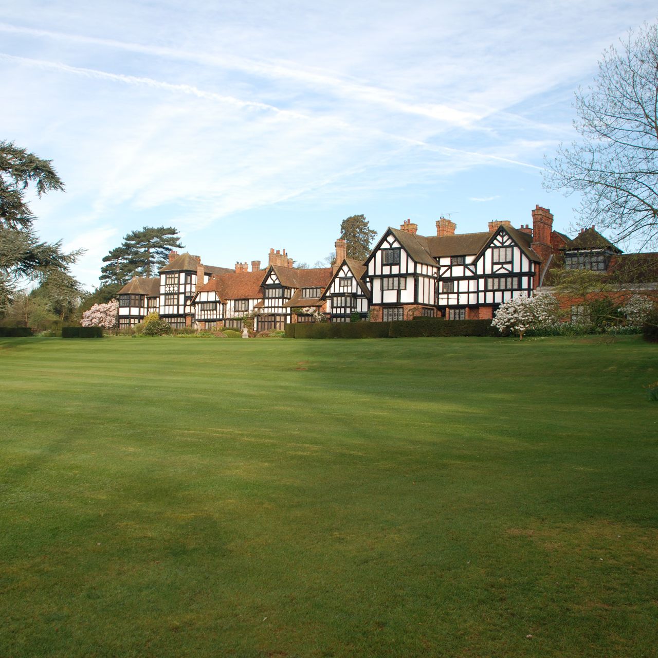 Large Tudor-style building with black and white timber framing, surrounded by a green lawn and trees.