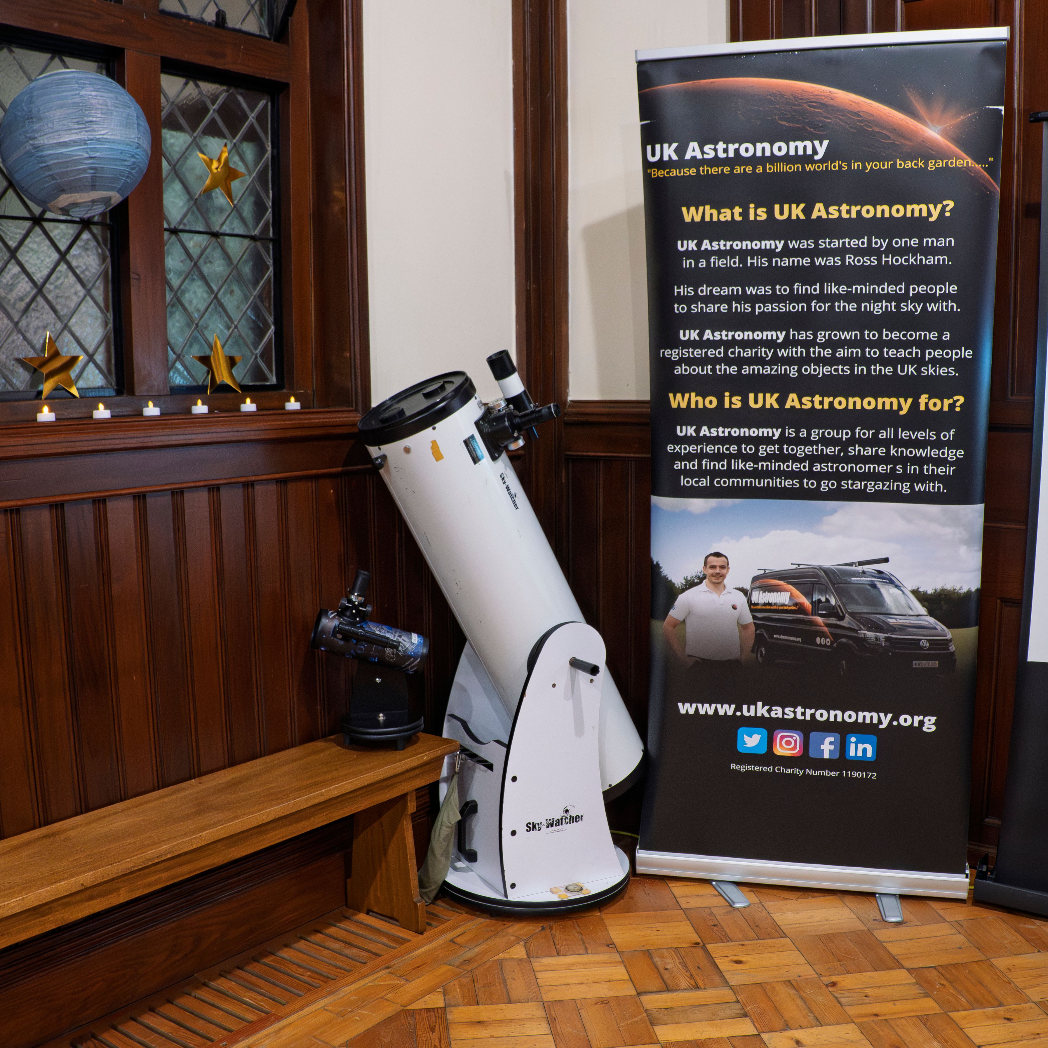 Indoor display with a large telescope beside a UK Astronomy information banner