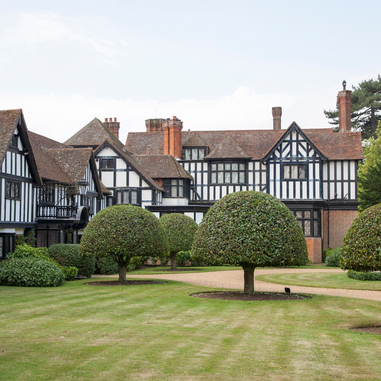 A large Tudor-style manor house with trimmed shrubbery and a manicured lawn in front.