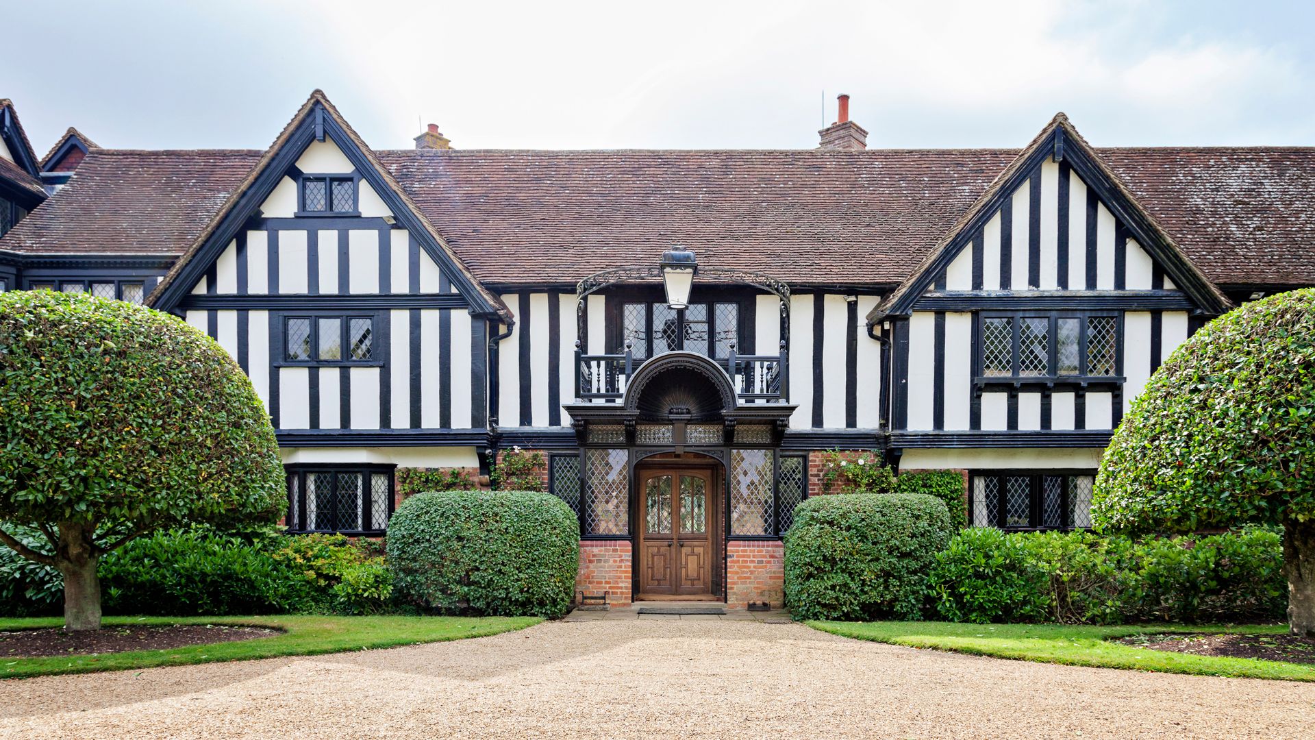 Traditional black and white Tudor-style house with gabled roof and trimmed hedges
