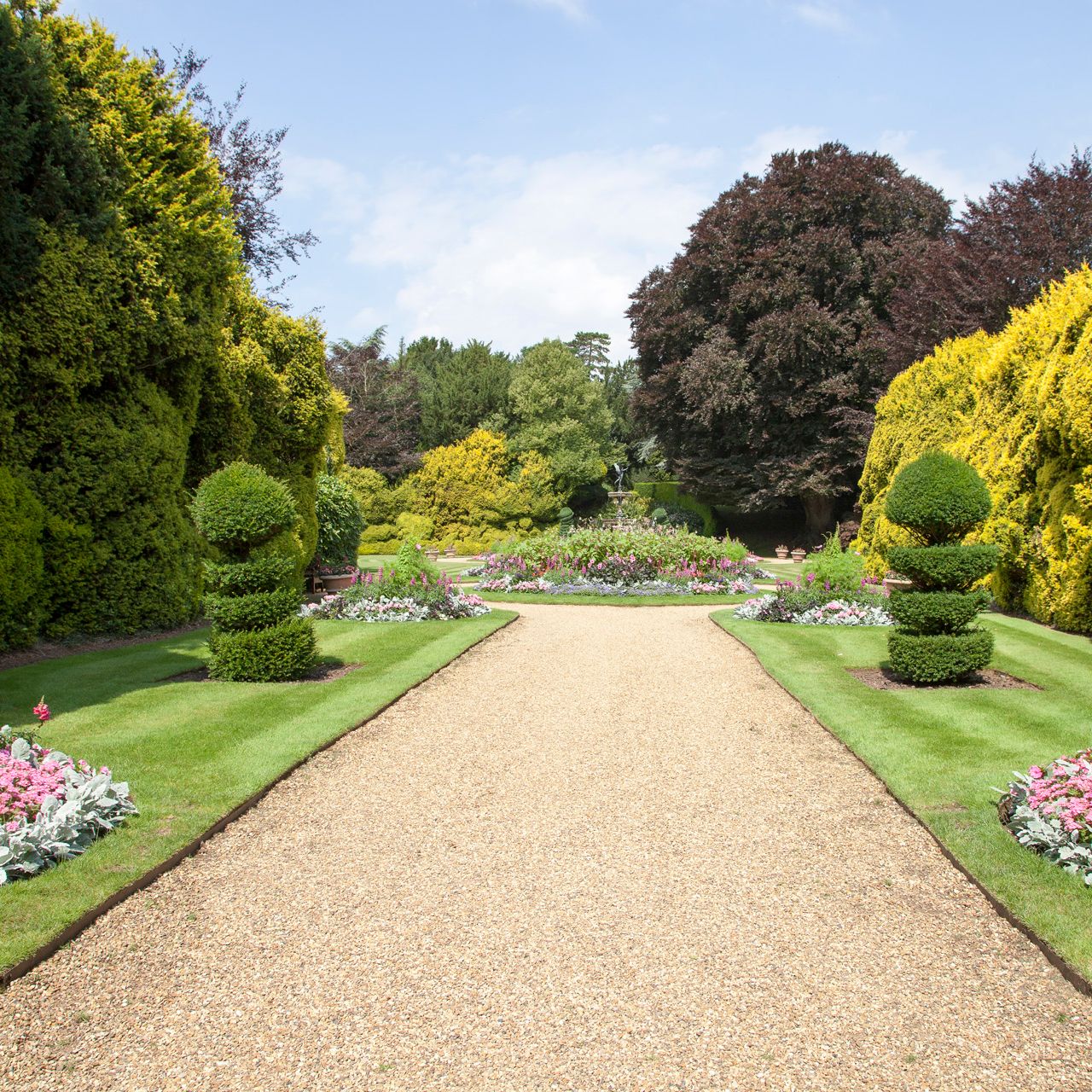A formal garden path lined with manicured shrubs, colorful flower beds, and neatly trimmed hedges.