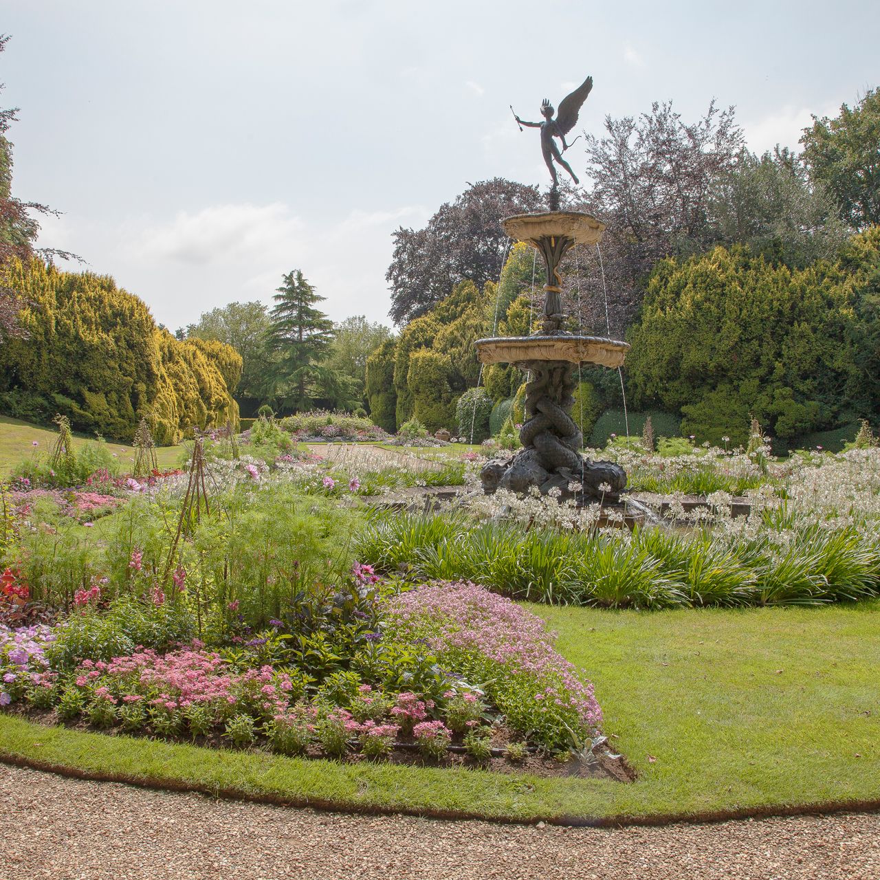 A landscaped garden with a flower bed and a decorative fountain featuring a statue at the center.