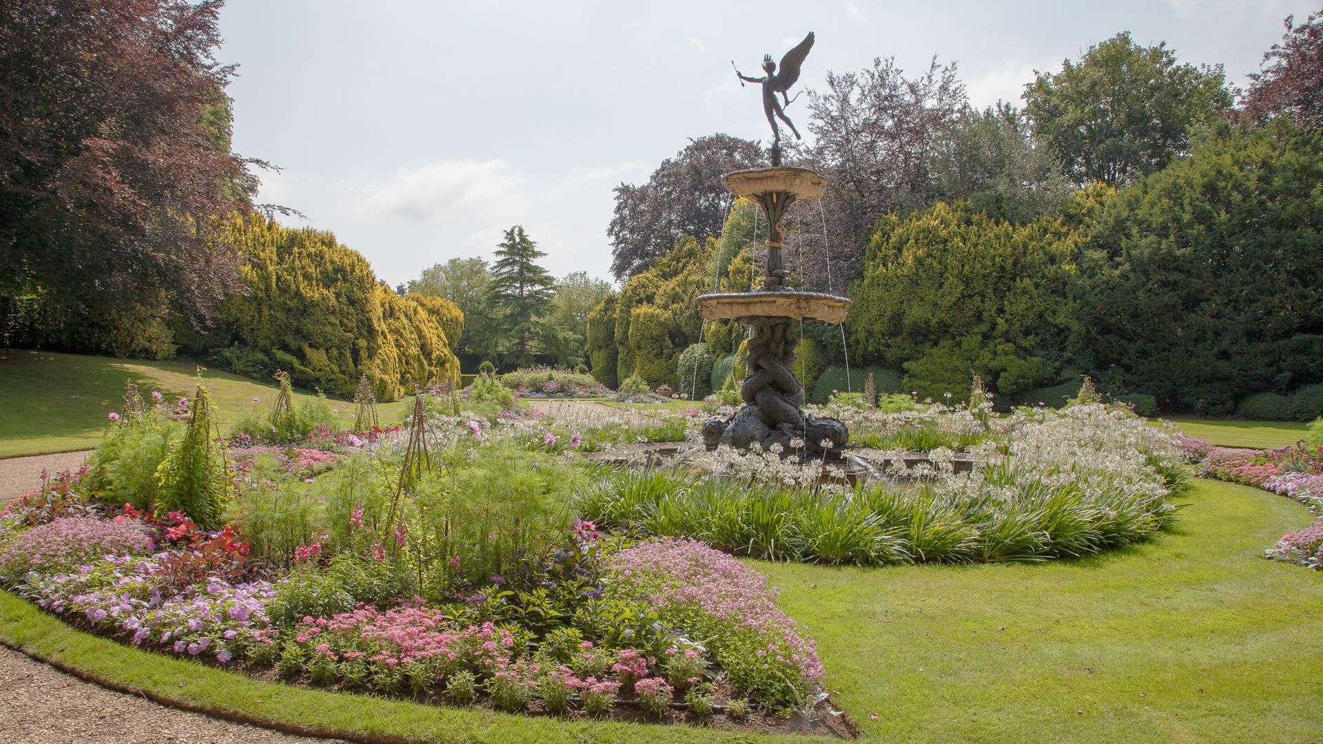 A landscaped garden with a flower bed and a decorative fountain featuring a statue at the center.