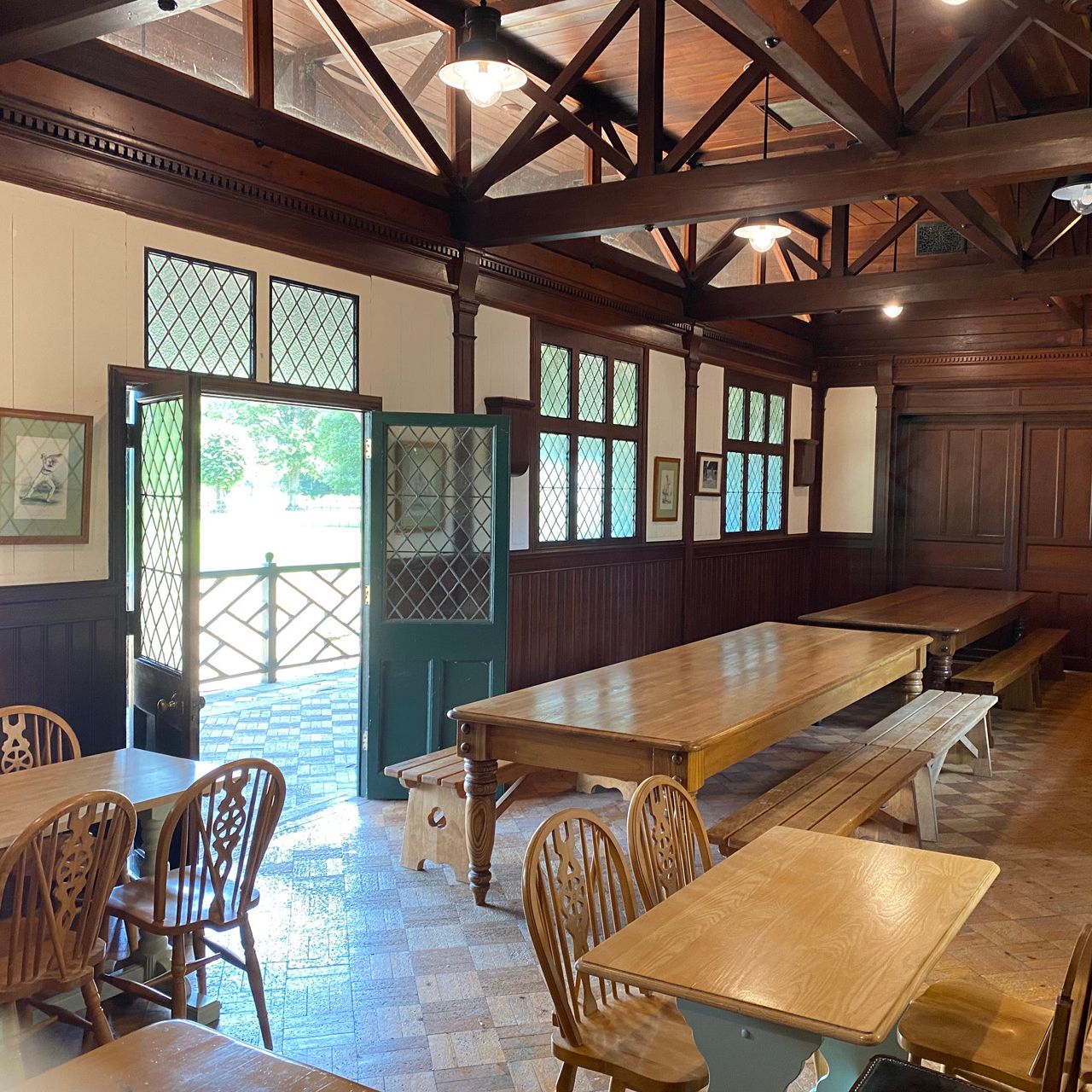Interior of a rustic dining room with wooden tables, chairs, benches, and open door letting in sunlight.