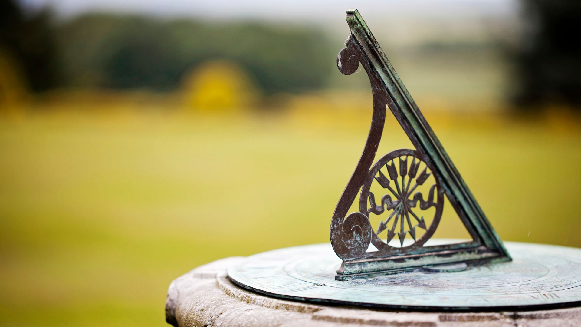 A close-up of an old metal sundial on a stone pedestal in a garden.