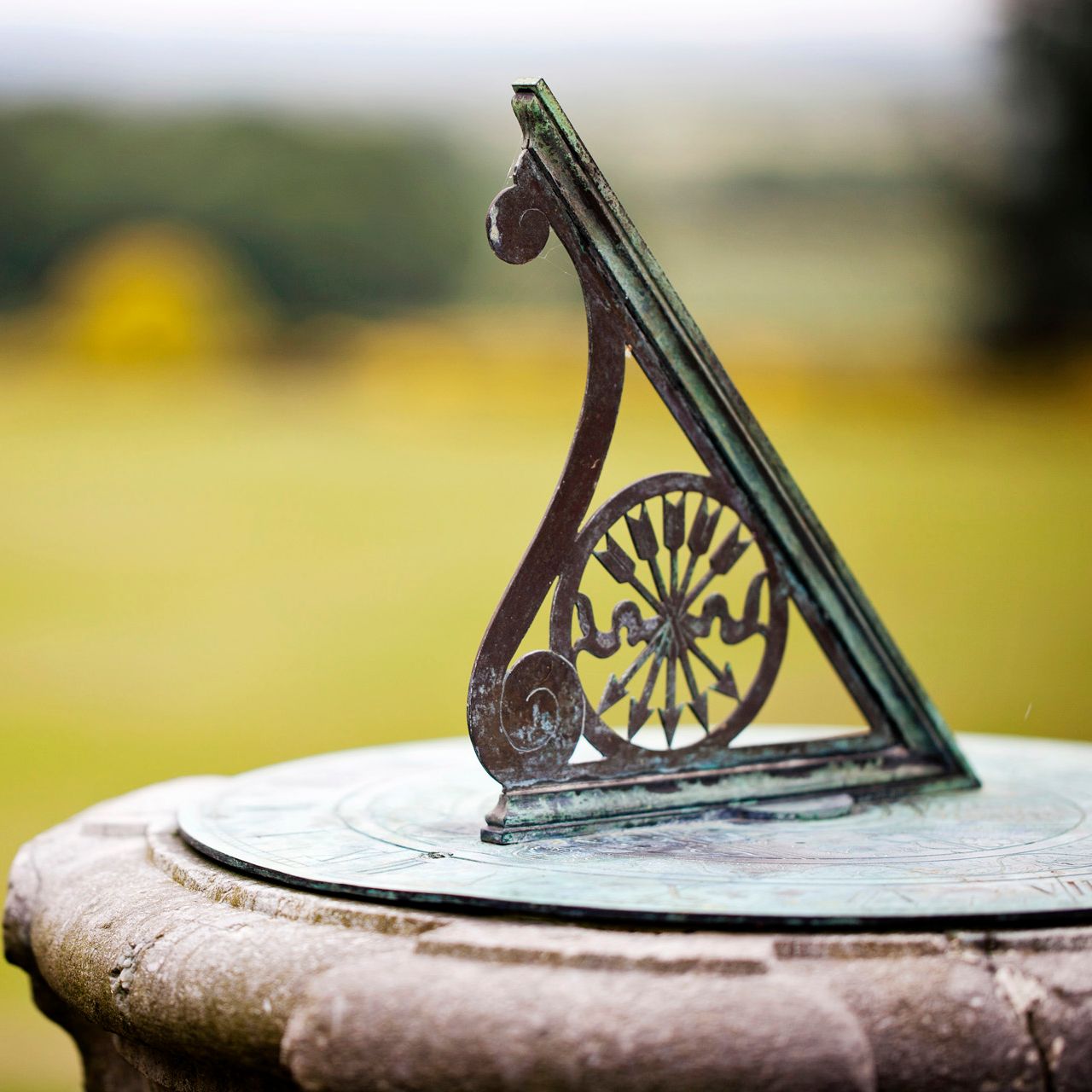 A close-up of an old metal sundial on a stone pedestal in a garden.