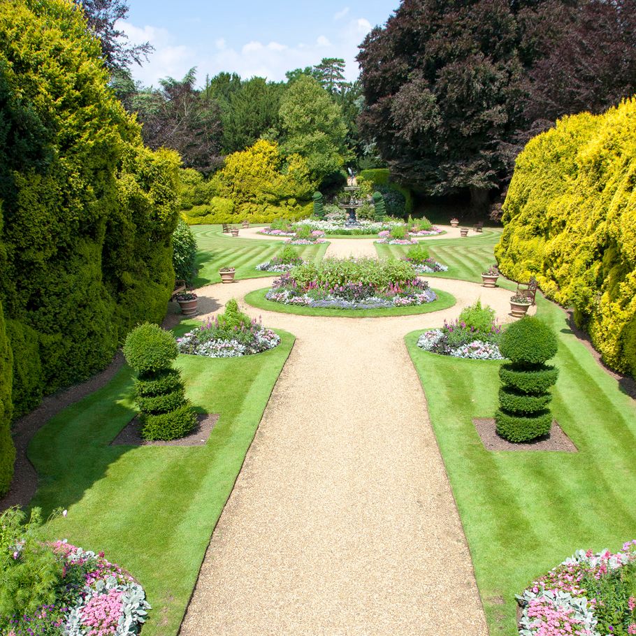 Well-manicured formal garden with symmetrical flower beds, trimmed hedges, and a central fountain.