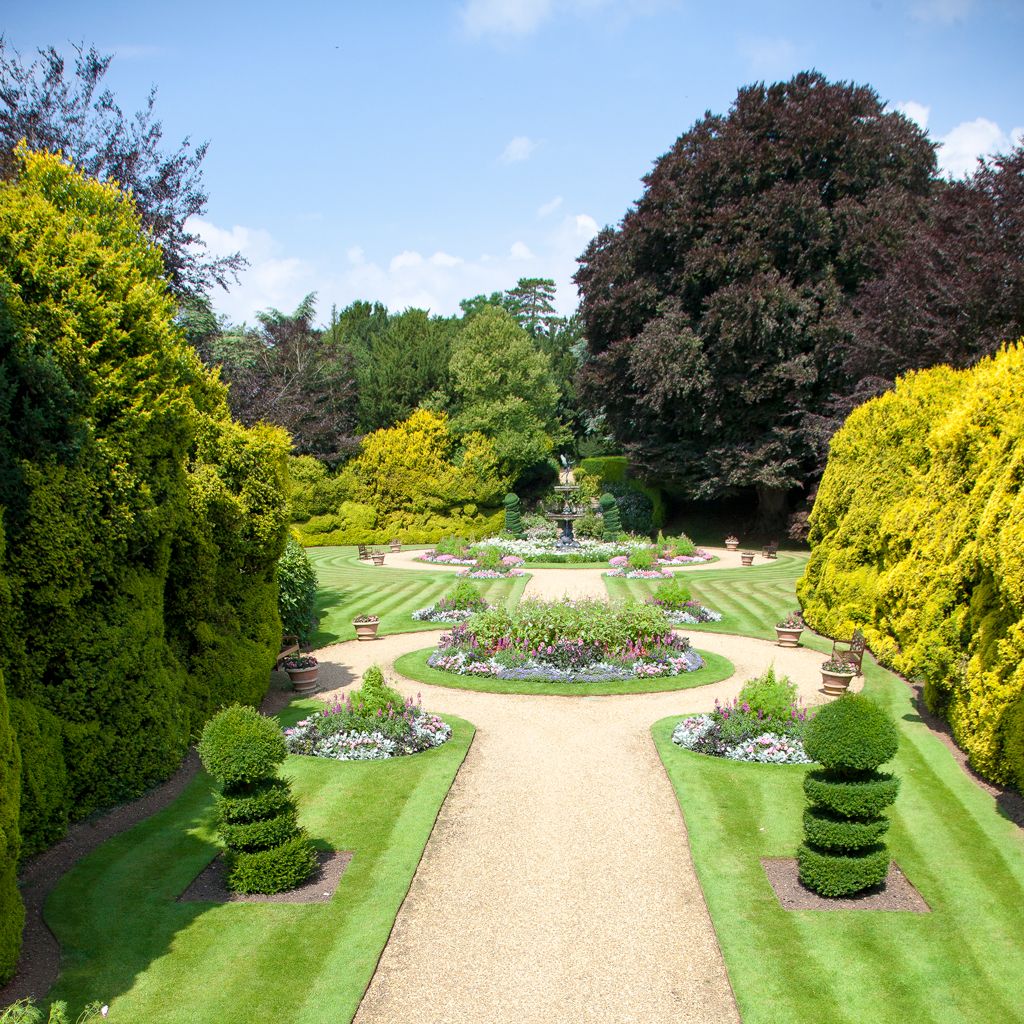 Beautiful formal garden with neatly trimmed lawns, colorful flower beds, and a central gravel path leading to a fountain.