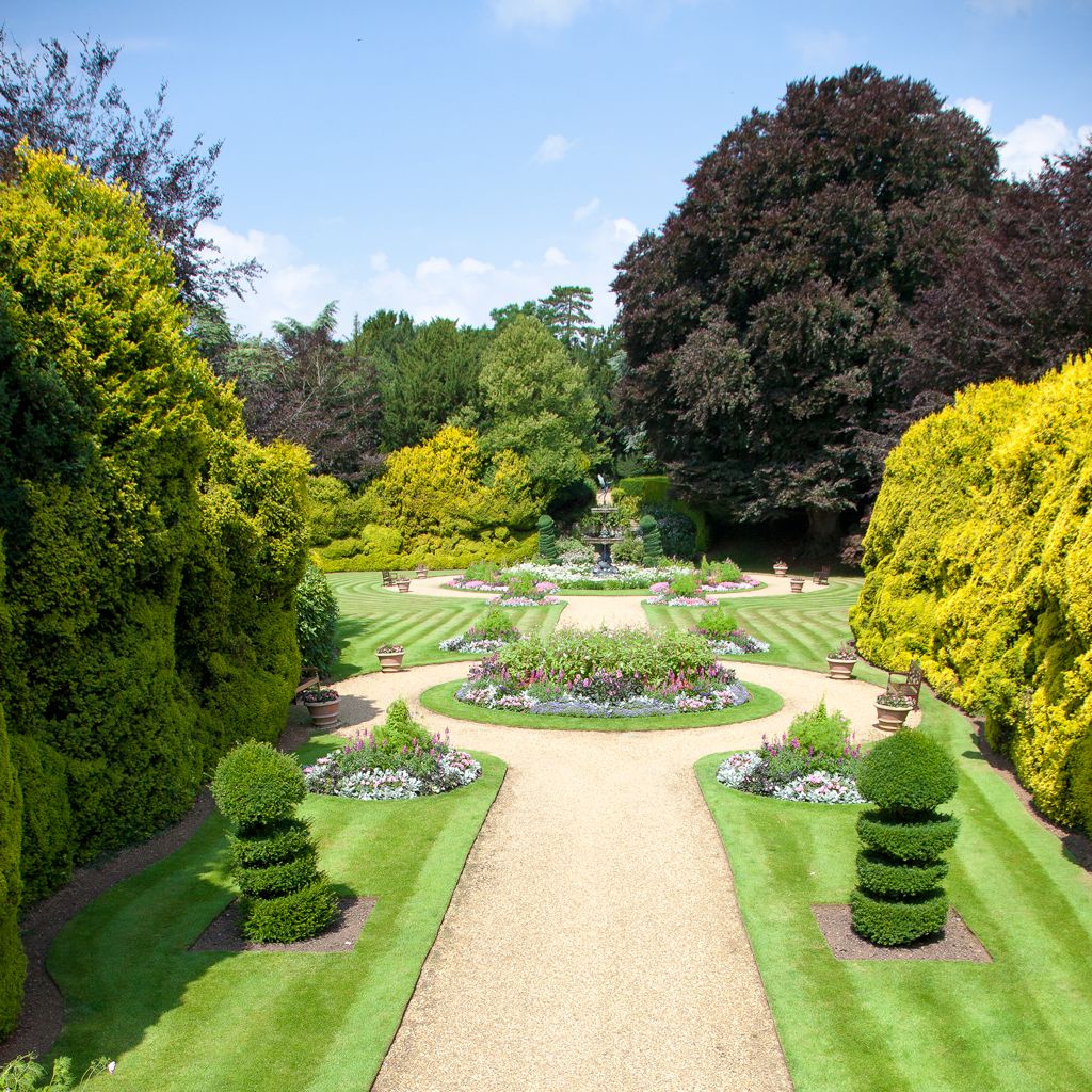 Beautiful formal garden with neatly trimmed lawns, colorful flower beds, and a central gravel path leading to a fountain.