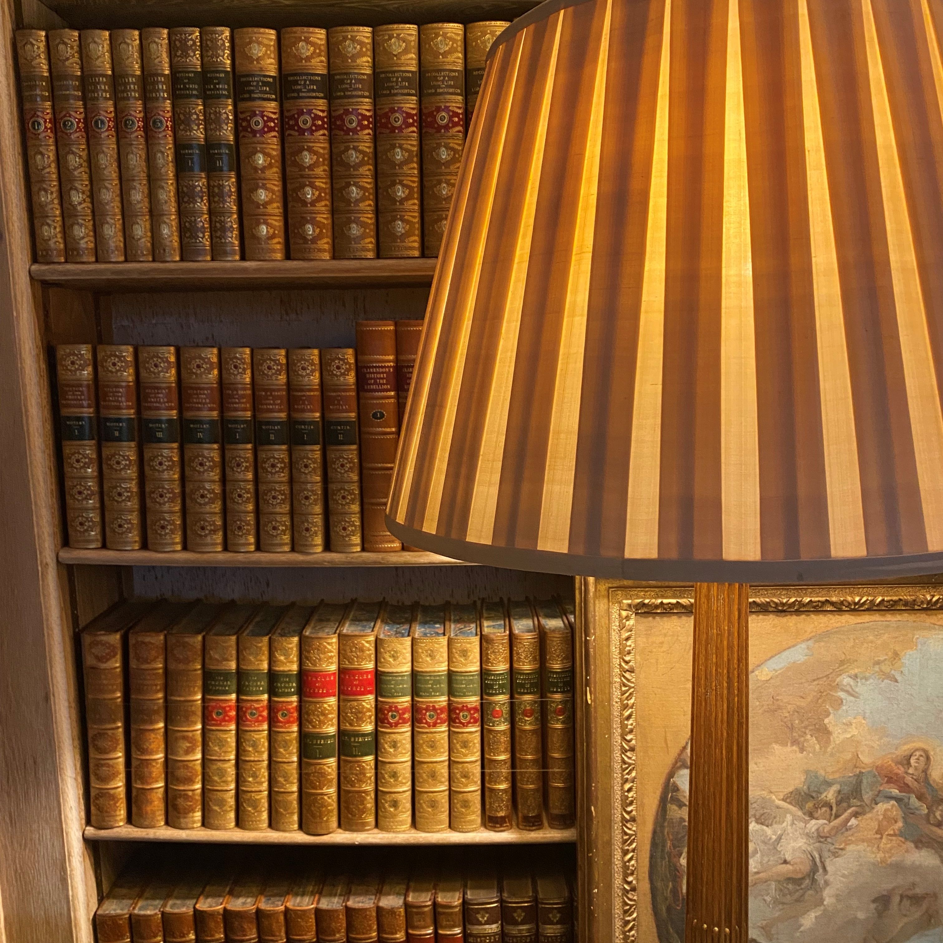 Bookshelf filled with antique books, a striped lampshade, and part of a painting