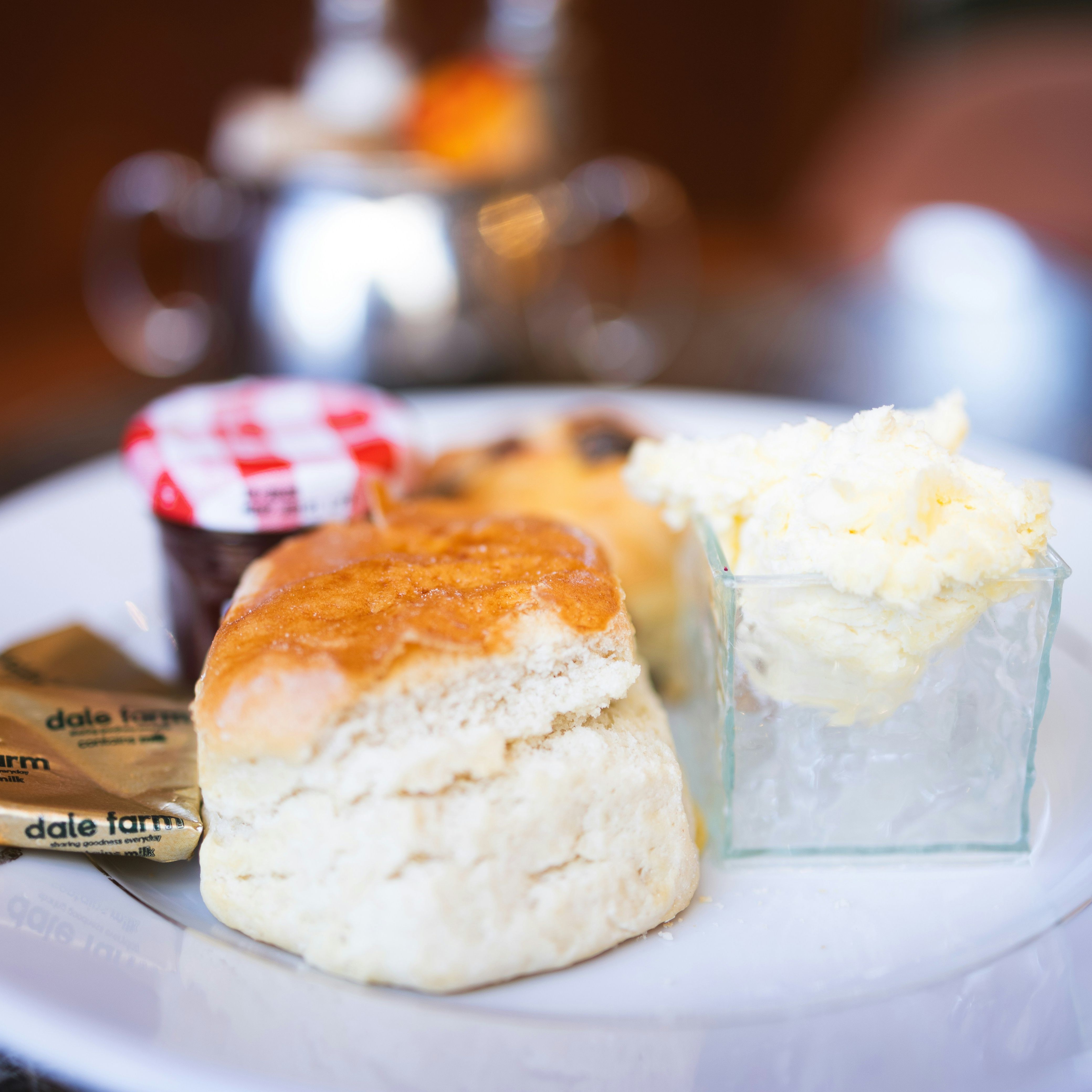 Close-up of a scone served with clotted cream, jam, and butter on a white plate.