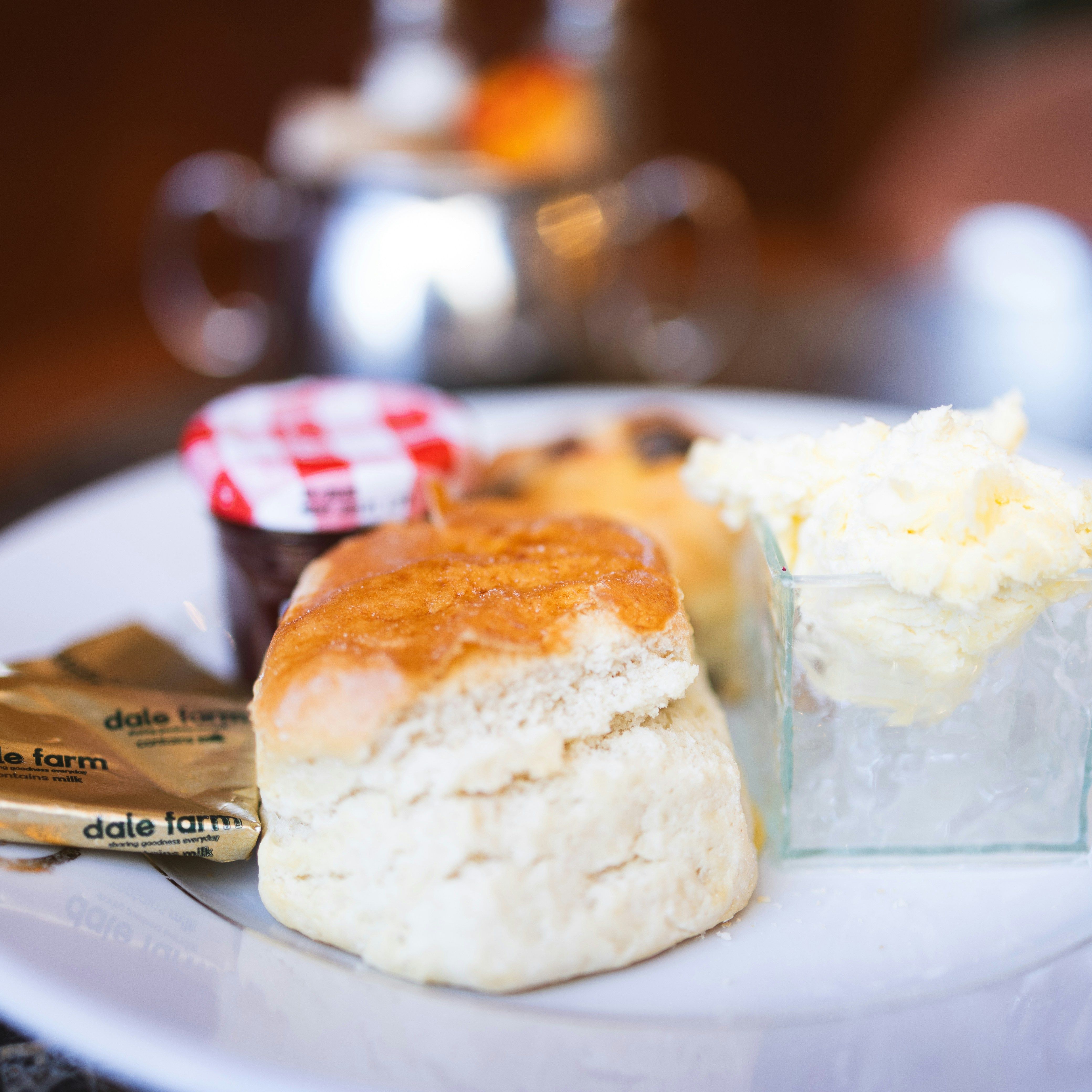 Close-up of a scone served with clotted cream, jam, and butter on a white plate.